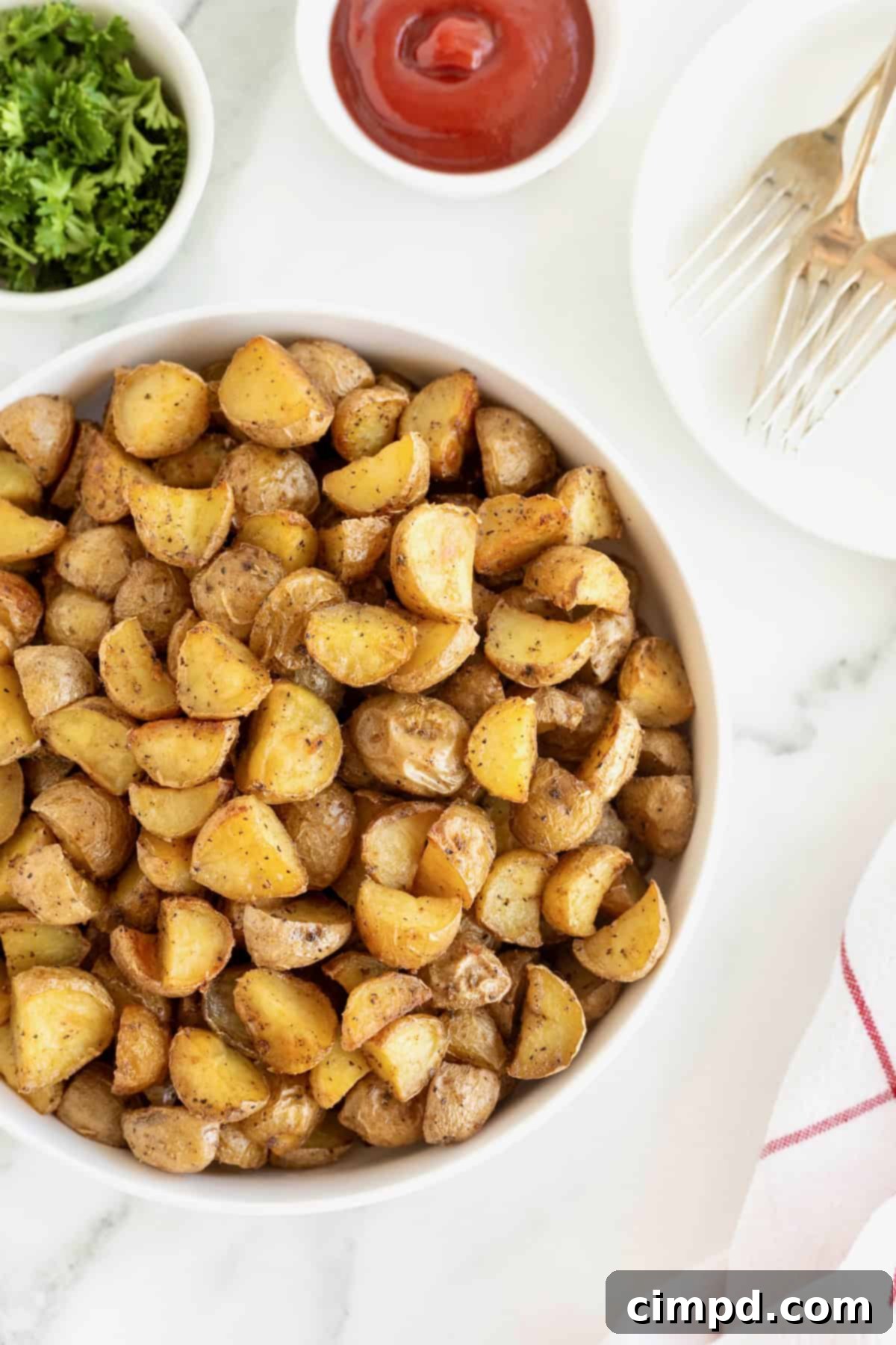 A large white serving dish of bite sized potato pieces on a white marble counter, garnished with fresh herbs.