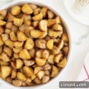 A large white serving dish of bite sized potato pieces on a white marble counter, showcasing Oven Roasted Crispy Potatoes.