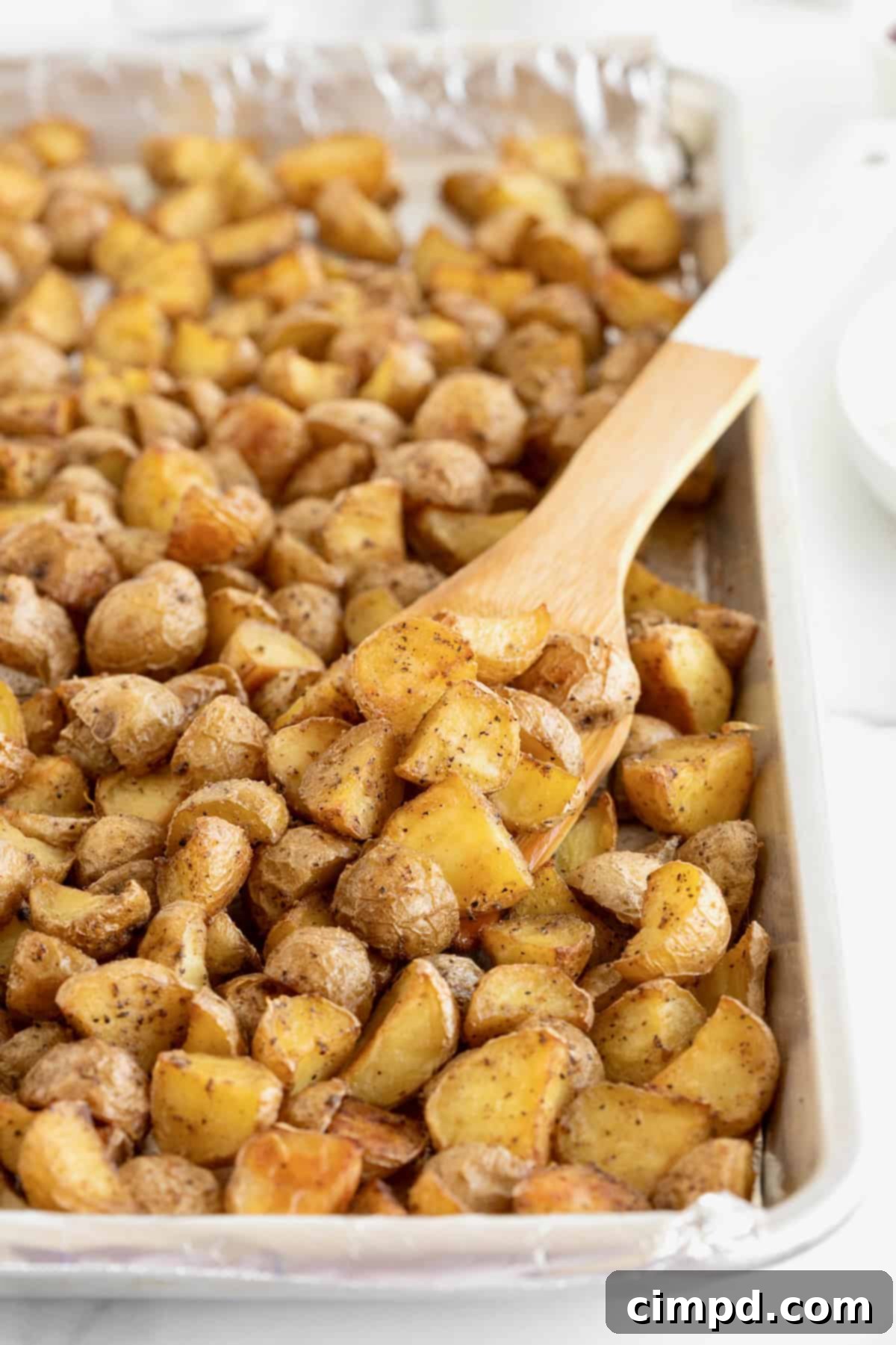 An aluminum baking sheet filled with perfectly oven roasted potatoes, with a wooden spatula resting on the side.