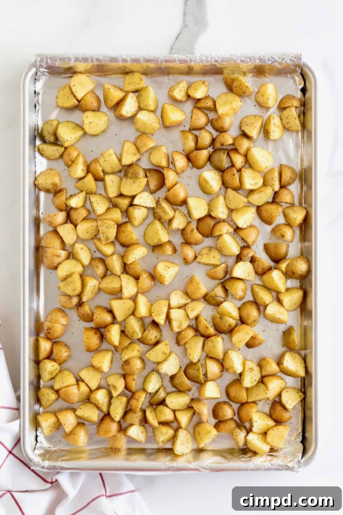 Raw quartered small potatoes arranged in a single, even layer on a foil-lined aluminum baking sheet, ready for roasting.
