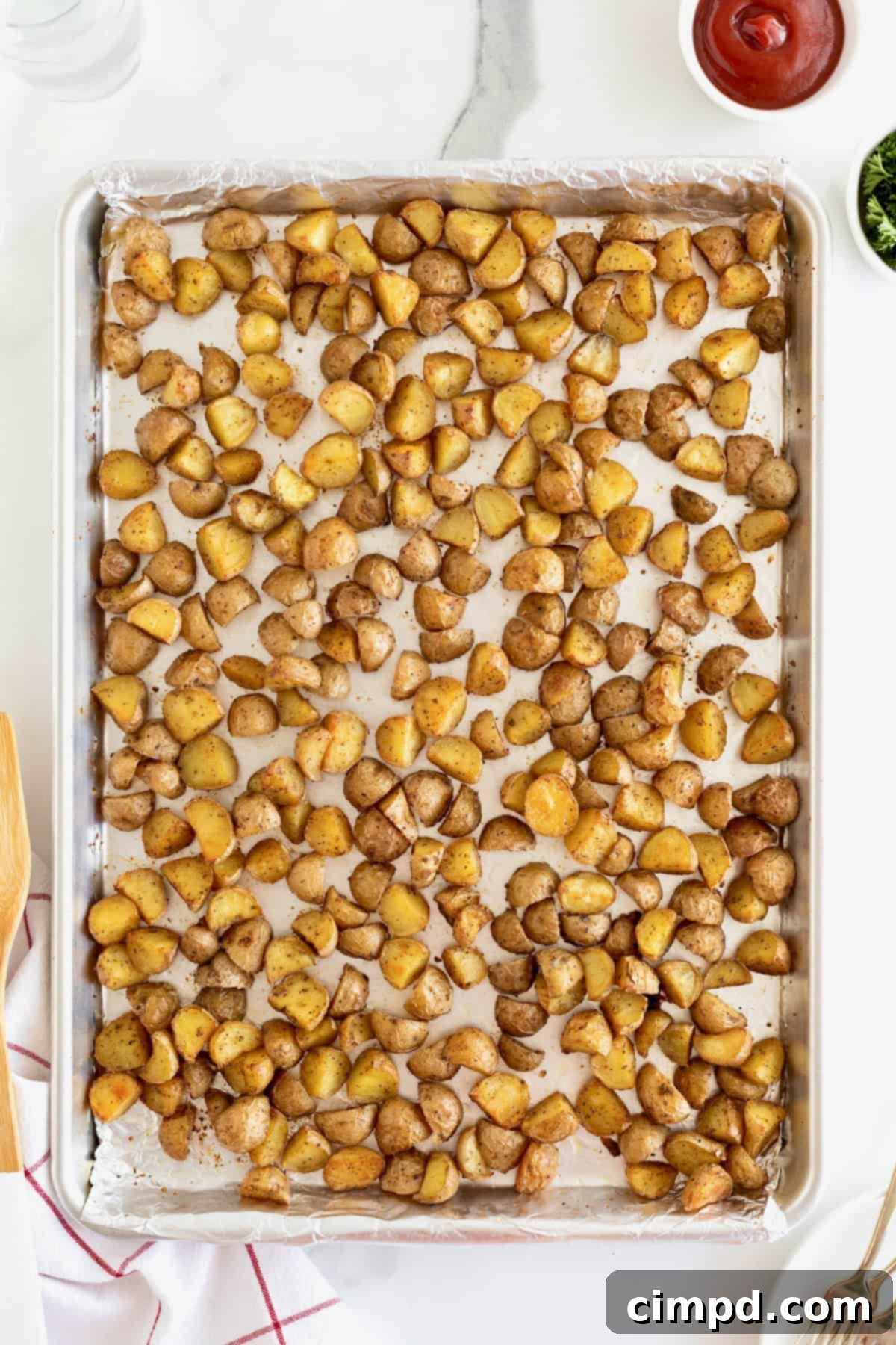Perfectly oven roasted quartered small potatoes, golden brown and crispy, spread out on a foil-lined aluminum baking sheet.