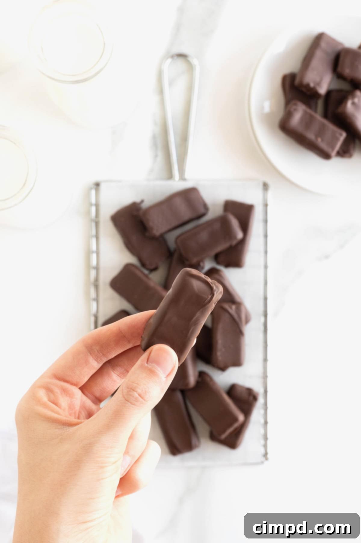 Quick Homemade KitKat Bites 3 A hand reaching for a homemade KitKat bite from a tempting pile on a parchment lined cooling rack, highlighting the perfect chocolate covering.