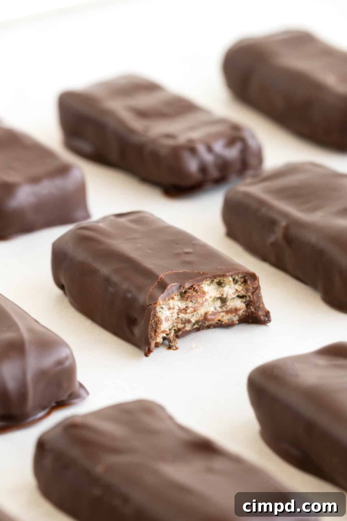Quick Homemade KitKat Bites 4 A close-up of homemade KitKat bites on a parchment lined cooling rack, with one bite taken out to reveal the crispy wafer layers.