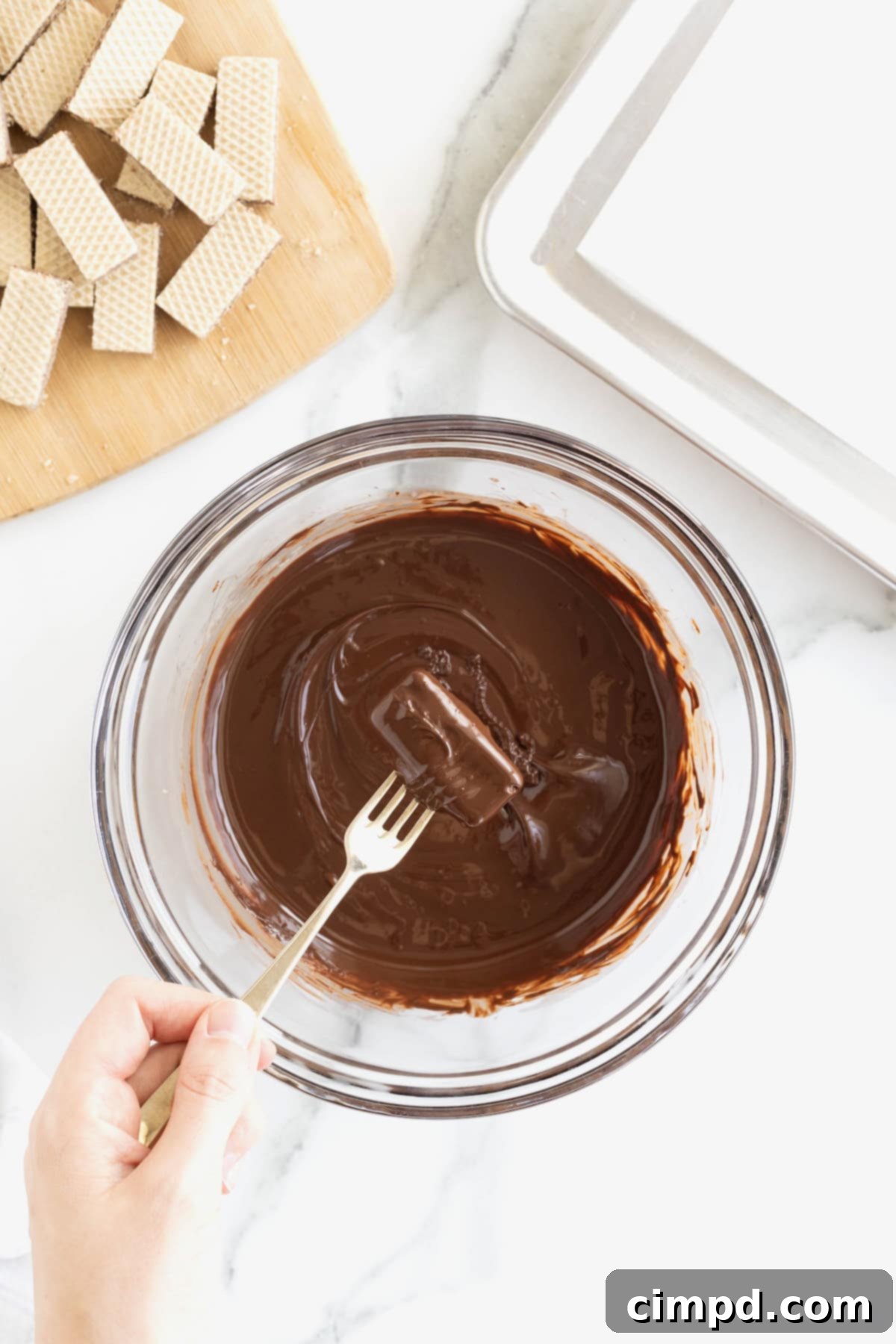 Quick Homemade KitKat Bites 8 A close-up shot of a fork delicately holding a mini KitKat bite, perfectly coated in melted chocolate, suspended just above a bowl of glossy chocolate.