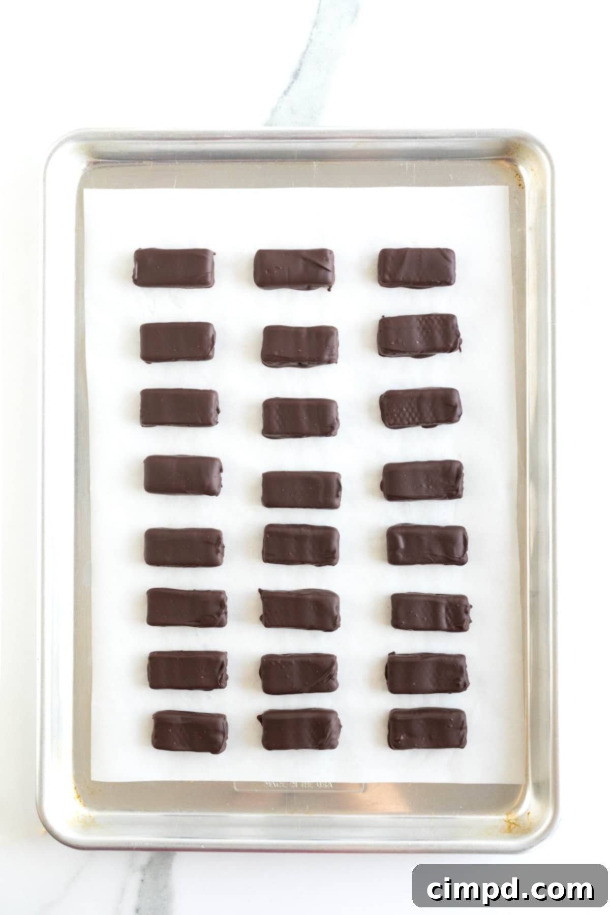 Quick Homemade KitKat Bites 10 A pristine display of 24 fully set homemade KitKat bites, their chocolate coating perfectly hardened, arranged on a parchment-lined aluminum baking sheet.