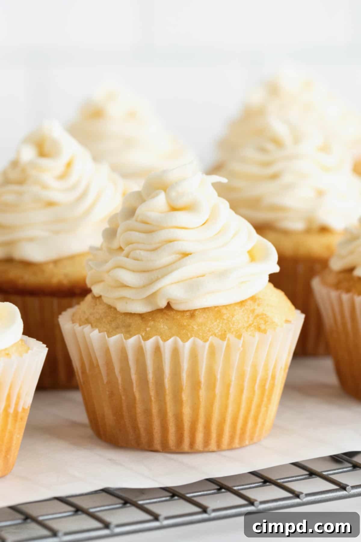Foolproof Buttercream Frosting 11 Six vanilla cupcakes piped with buttercream frosting sitting on a parchment lined cooling rack.