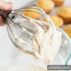 Foolproof Buttercream Frosting 13 A hand holding the whisk attachment from an electric mixer with white buttercream frosting on it.