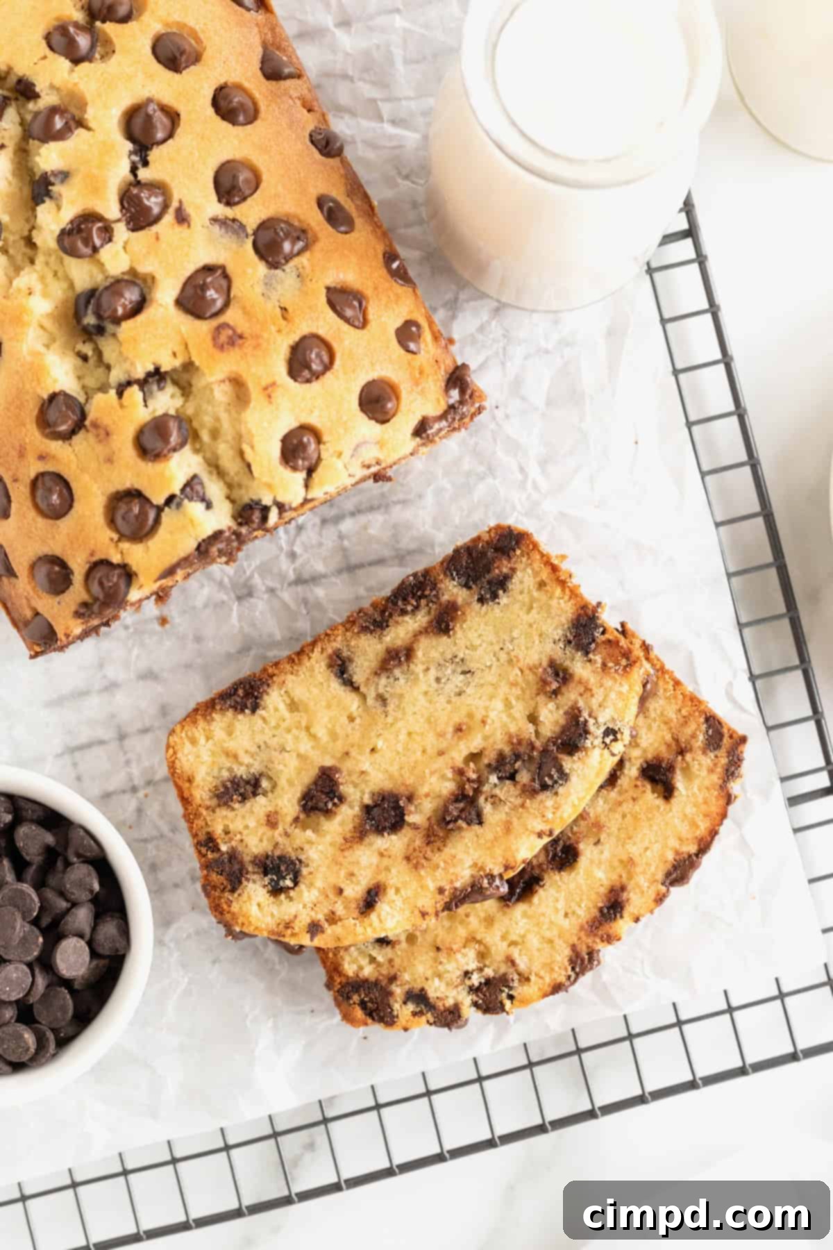 Decadent Chocolate Chip Pound Cake 2 A slice of chocolate chip pound cake in front of a loaf of pound cake on a parchment lined cooling rack. A small white dish of chocolate chips sits to the bottom left of the photo.