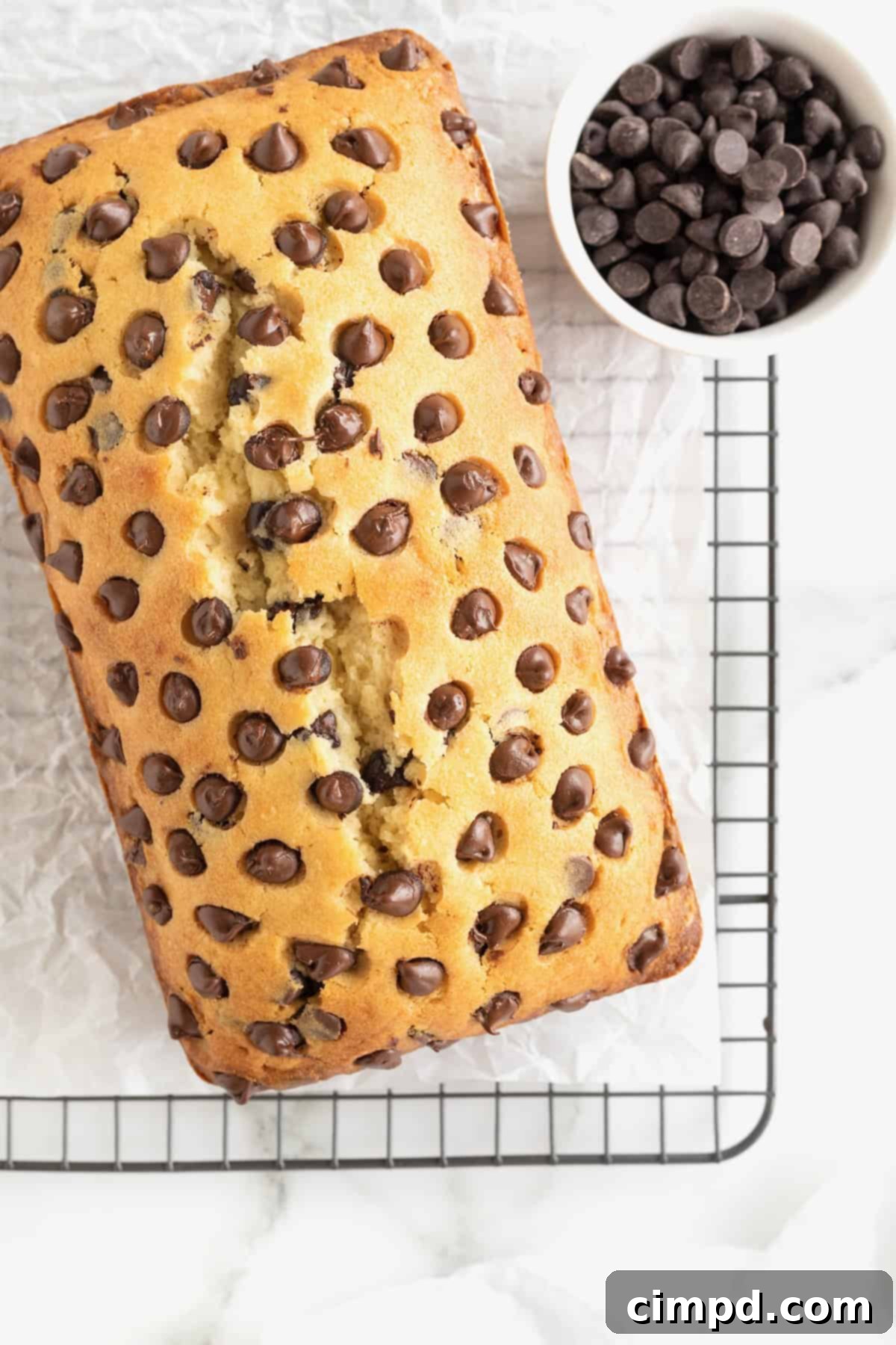 Decadent Chocolate Chip Pound Cake 4 A loaf of Chocolate Chip Pound Cake on a parchment lined cooling rack. A small white dish of chocolate chips sits to the top right corner.