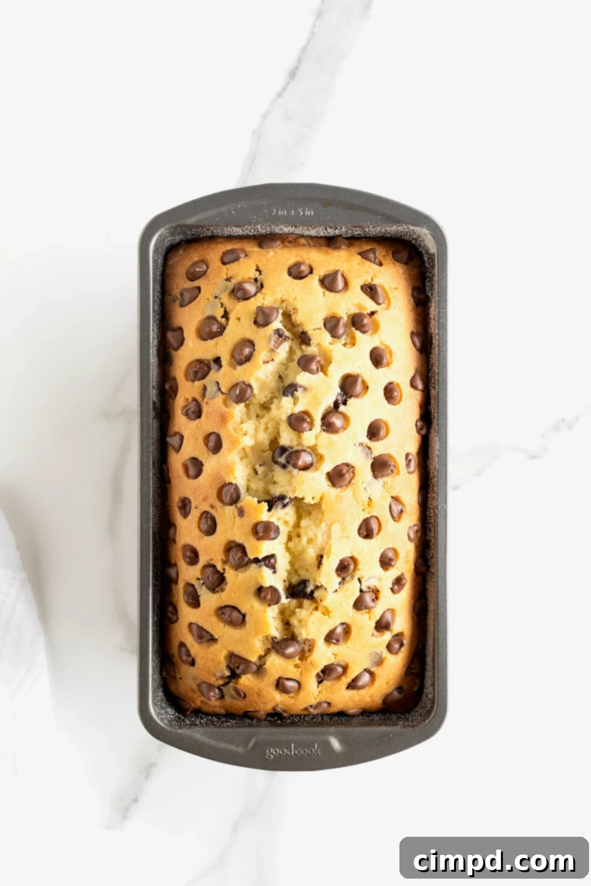 Decadent Chocolate Chip Pound Cake 8 Chocolate chip pound cake in a dark metal loaf pan on a white marble counter.
