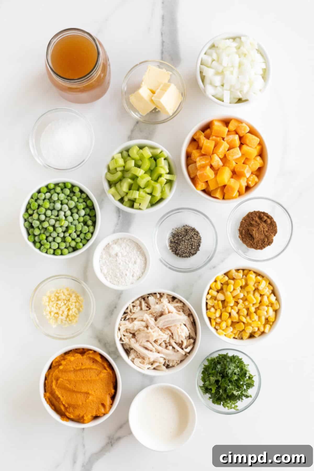 Various ingredients for pumpkin pot pie soup meticulously arranged in small glass dishes on a pristine white marble counter, showcasing their freshness and readiness for cooking.