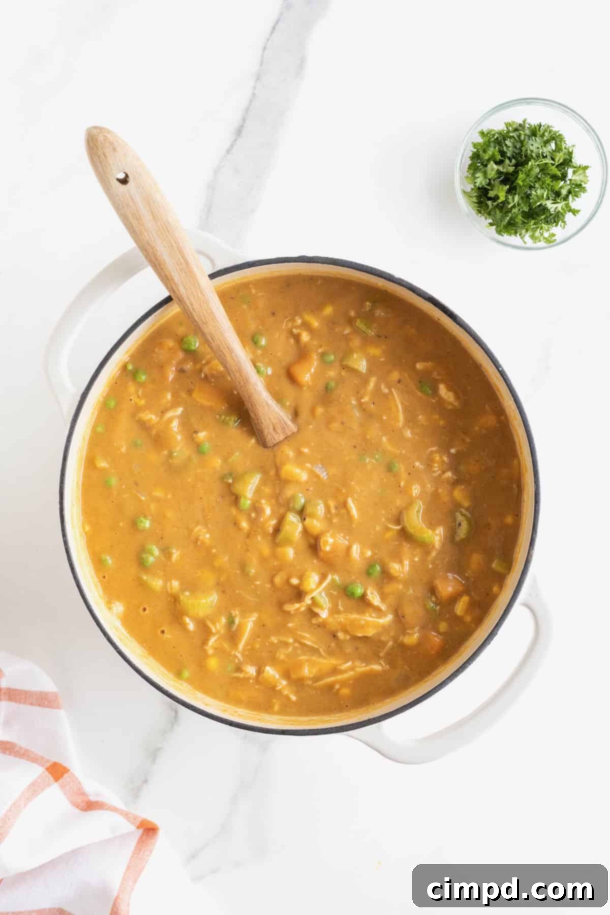 A pristine white Dutch oven, brimming with hot and inviting Pumpkin Pot Pie Soup, sits on a smooth white marble countertop, ready to be served.