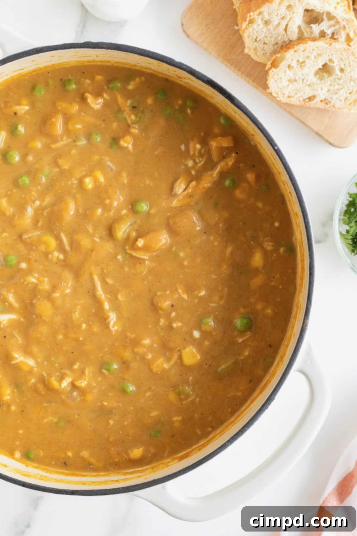 A pristine white Dutch oven, filled with a delicious pumpkin pot pie soup, rests on a gleaming white marble countertop.