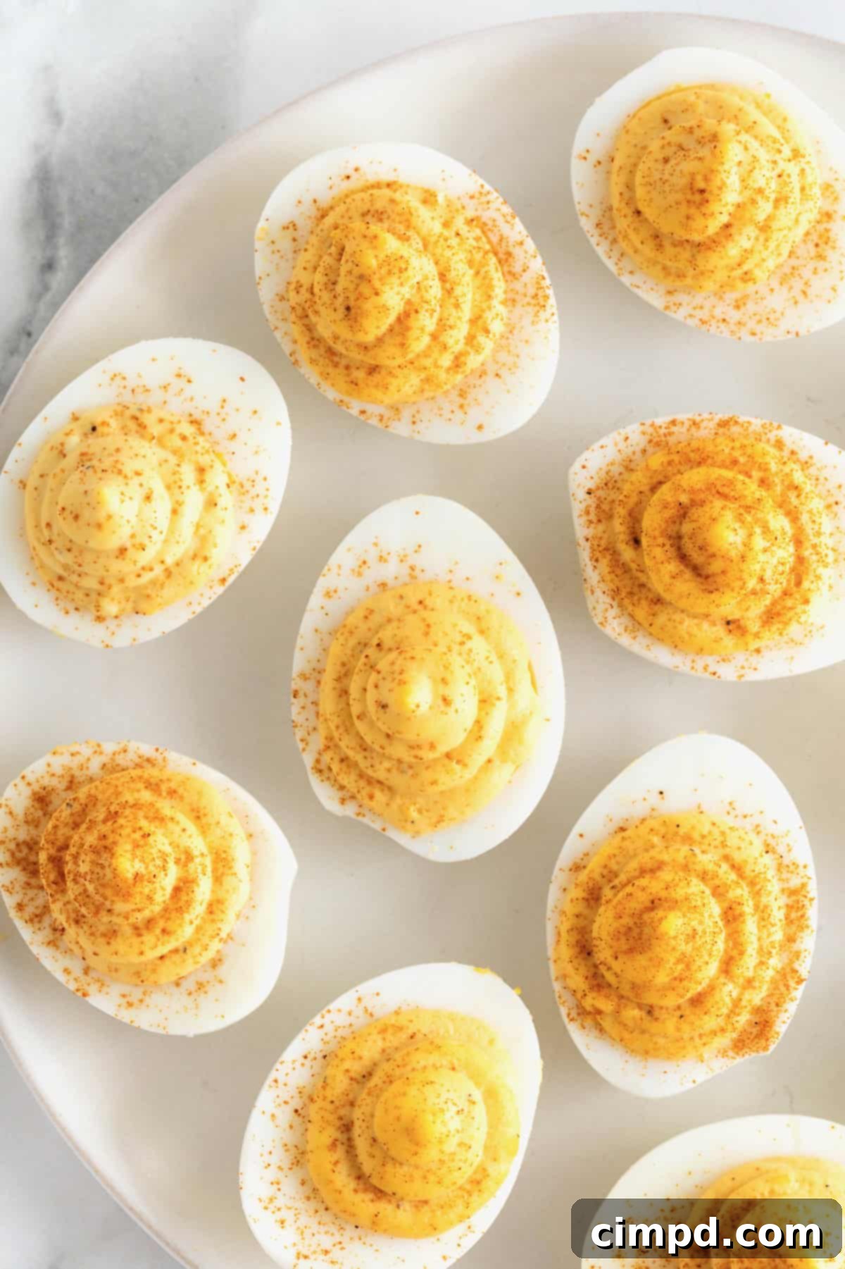 Devilish Delights 2 A large white serving platter filled with beautifully arranged classic deviled eggs, garnished with paprika, resting on a clean white marble counter.