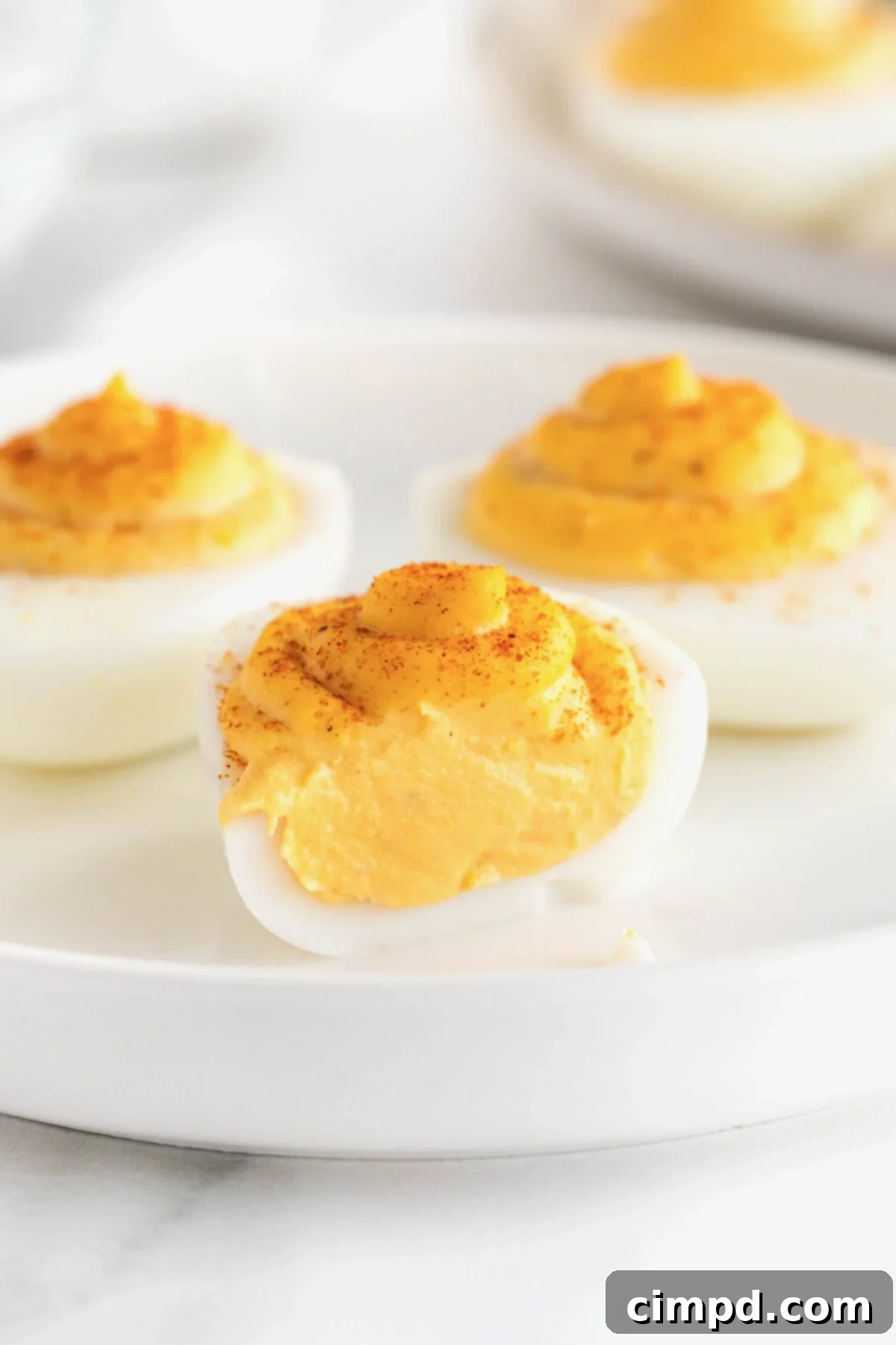 Devilish Delights 3 Three perfectly prepared deviled eggs, one cut in half to reveal the creamy yolk filling, elegantly presented on a white rimmed plate.