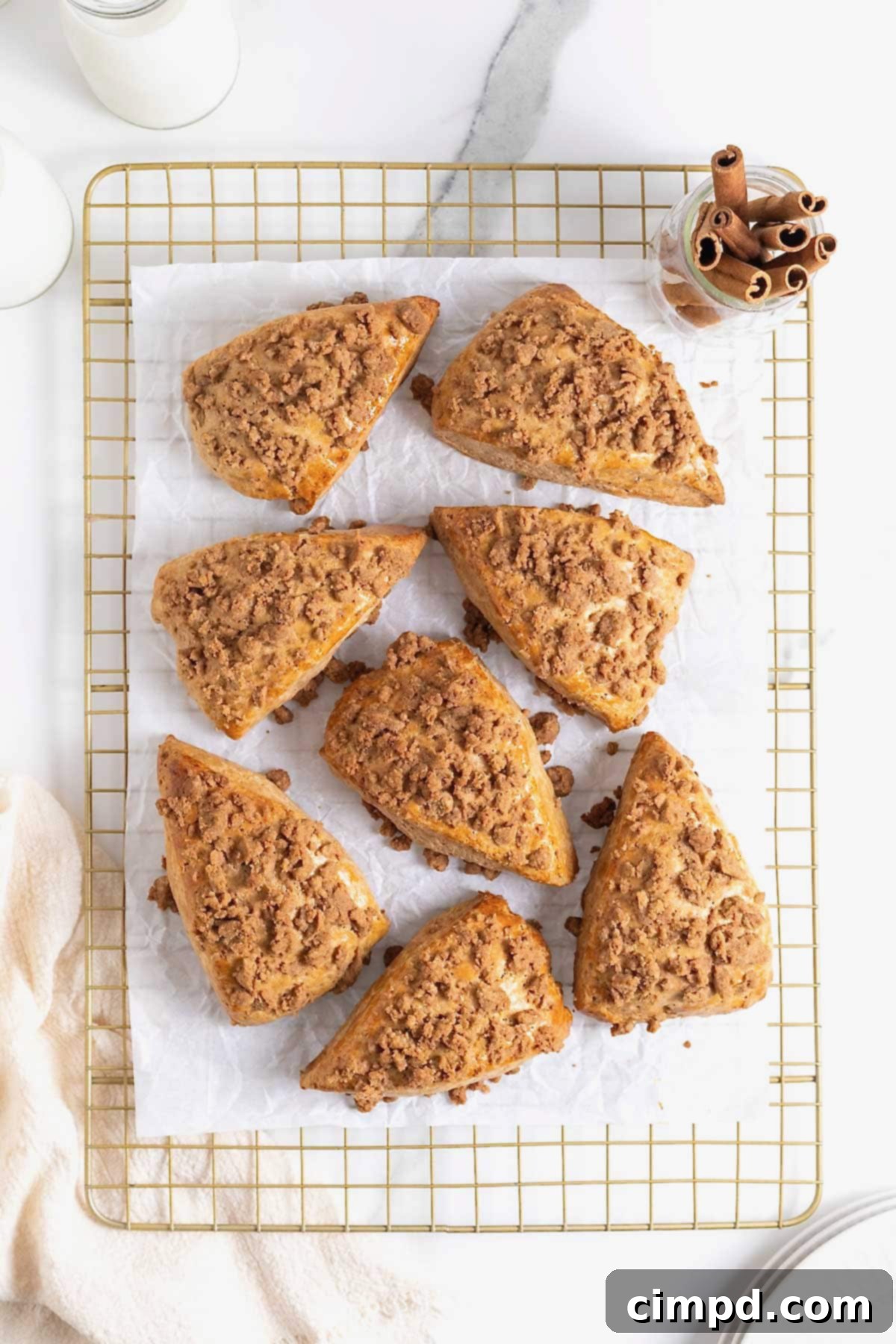 Eight delicious snickerdoodle streusel scones cooling on a gold-toned wire rack, still on parchment paper.