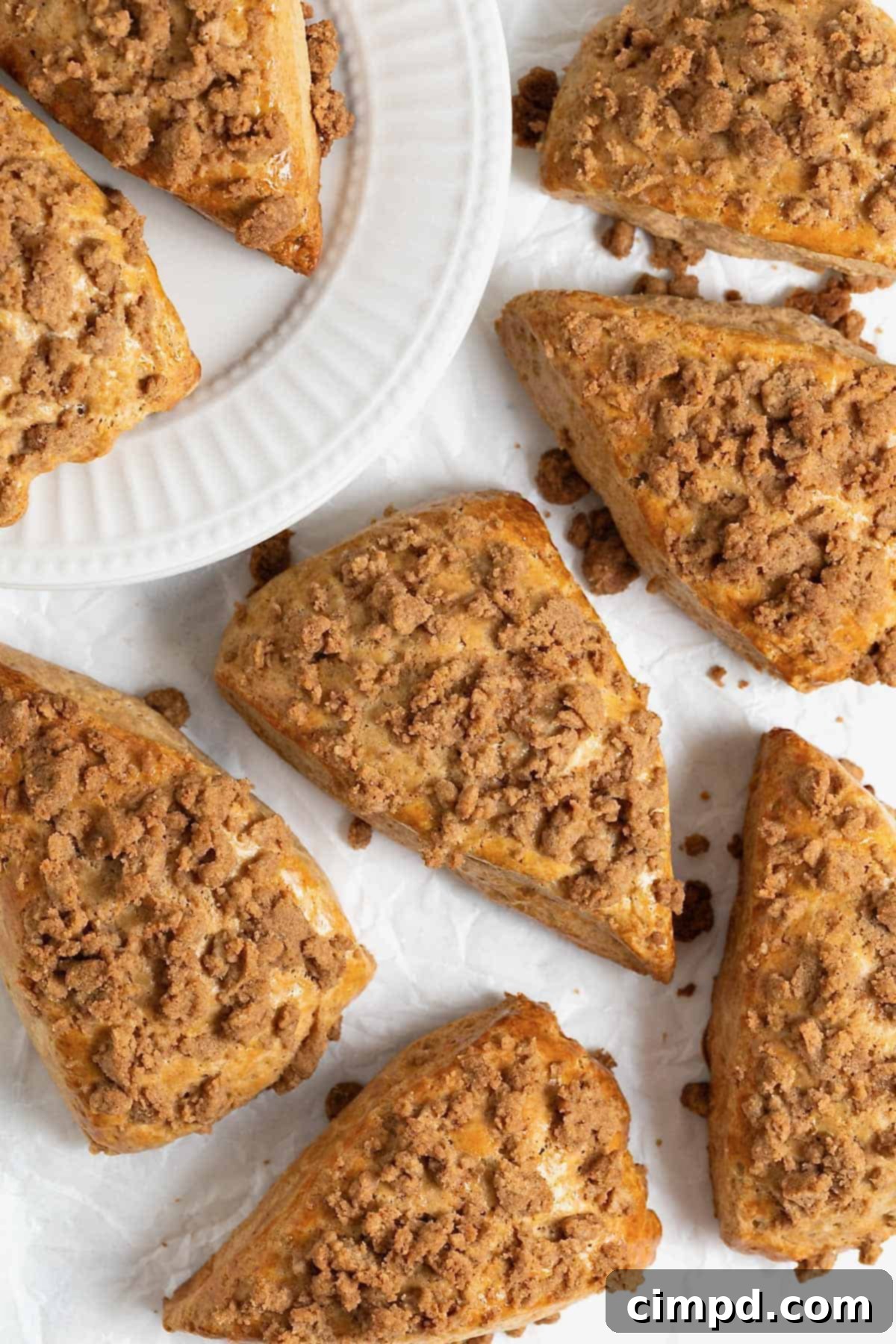 A charming arrangement of five snickerdoodle streusel scones on a white surface, with two more on a white plate in the background.