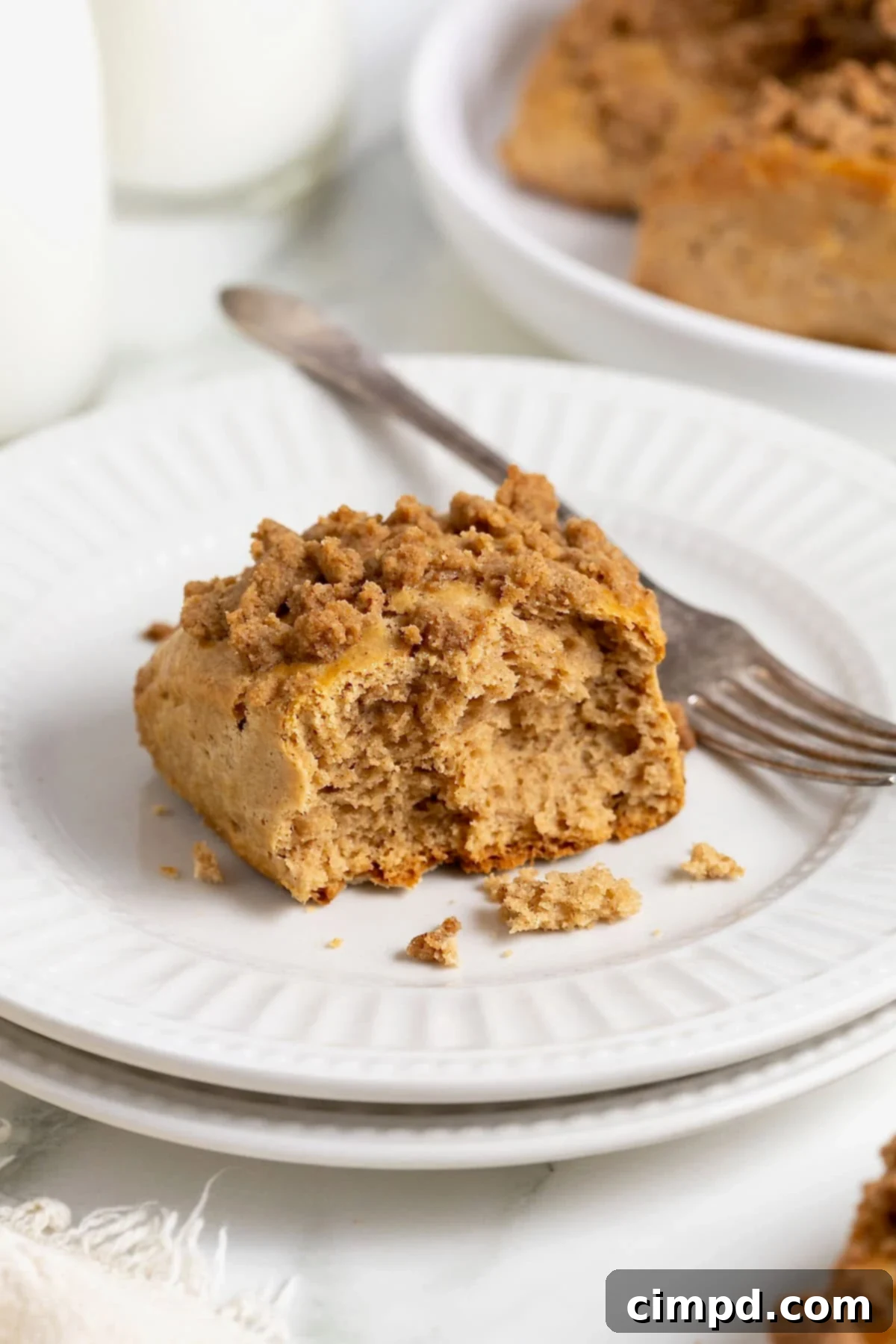 A single snickerdoodle scone, with a bite taken, rests on a white fluted plate with a fork nearby.
