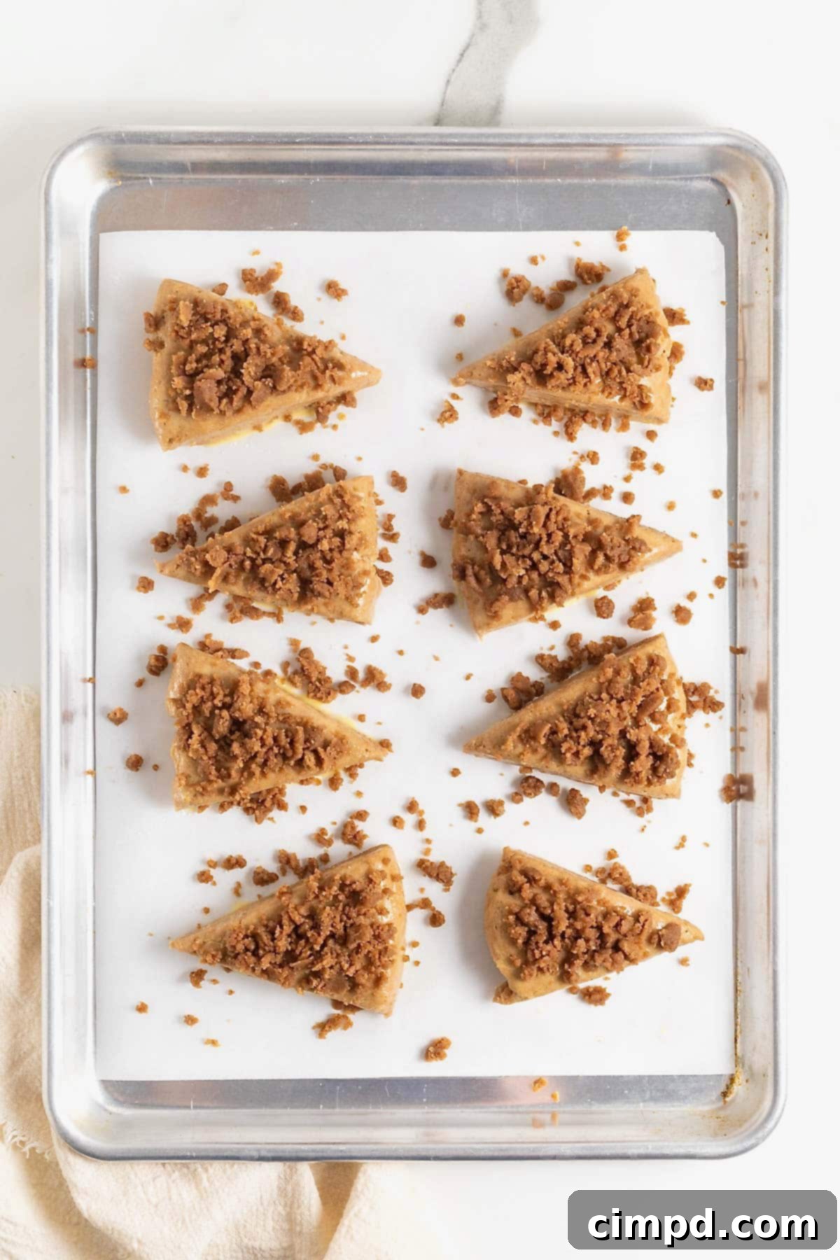 Scones on a parchment-lined baking sheet, generously topped with cinnamon sugar streusel, ready for the oven.