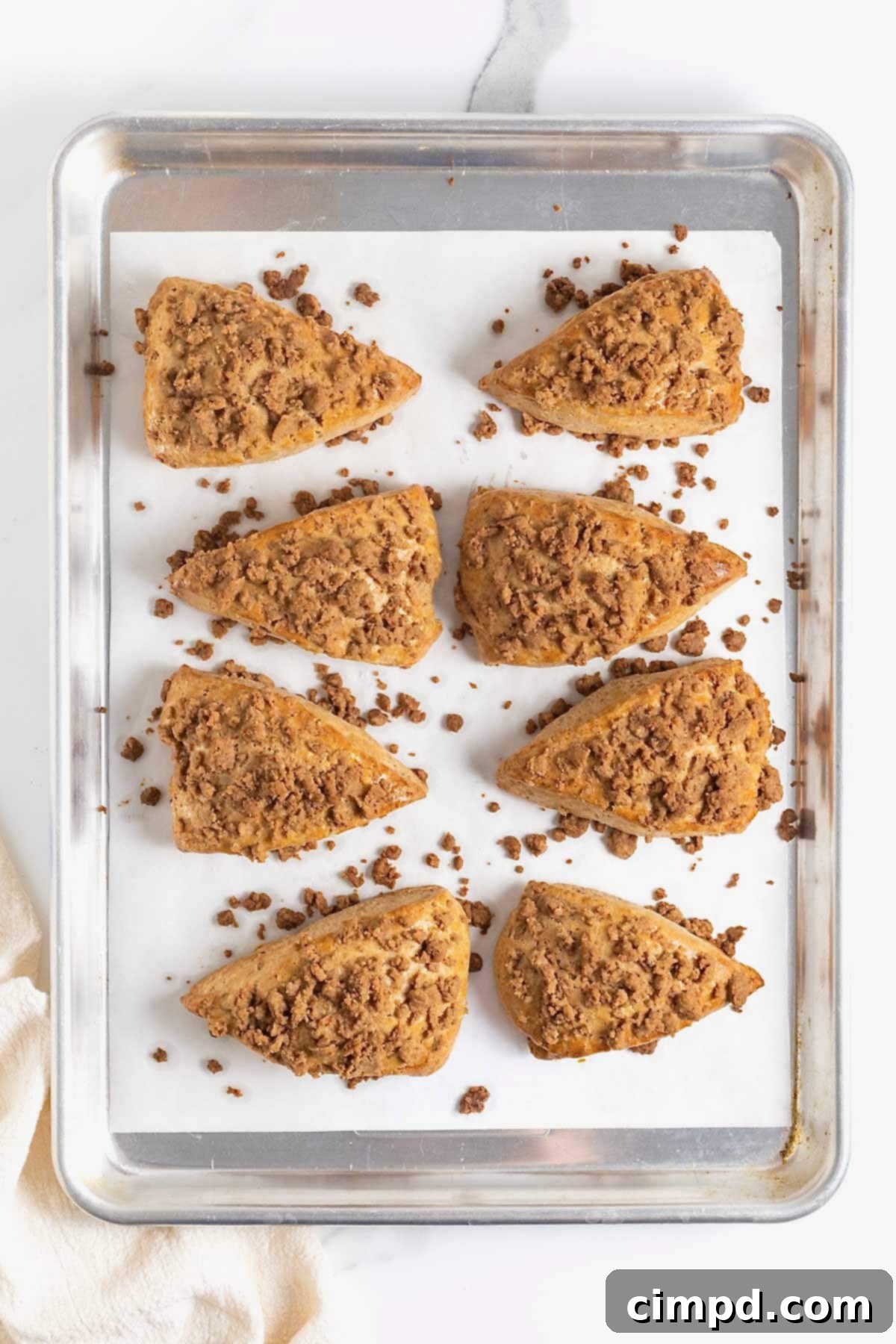 Eight perfectly baked snickerdoodle streusel scones, golden brown and glistening, resting on a parchment-lined baking sheet.