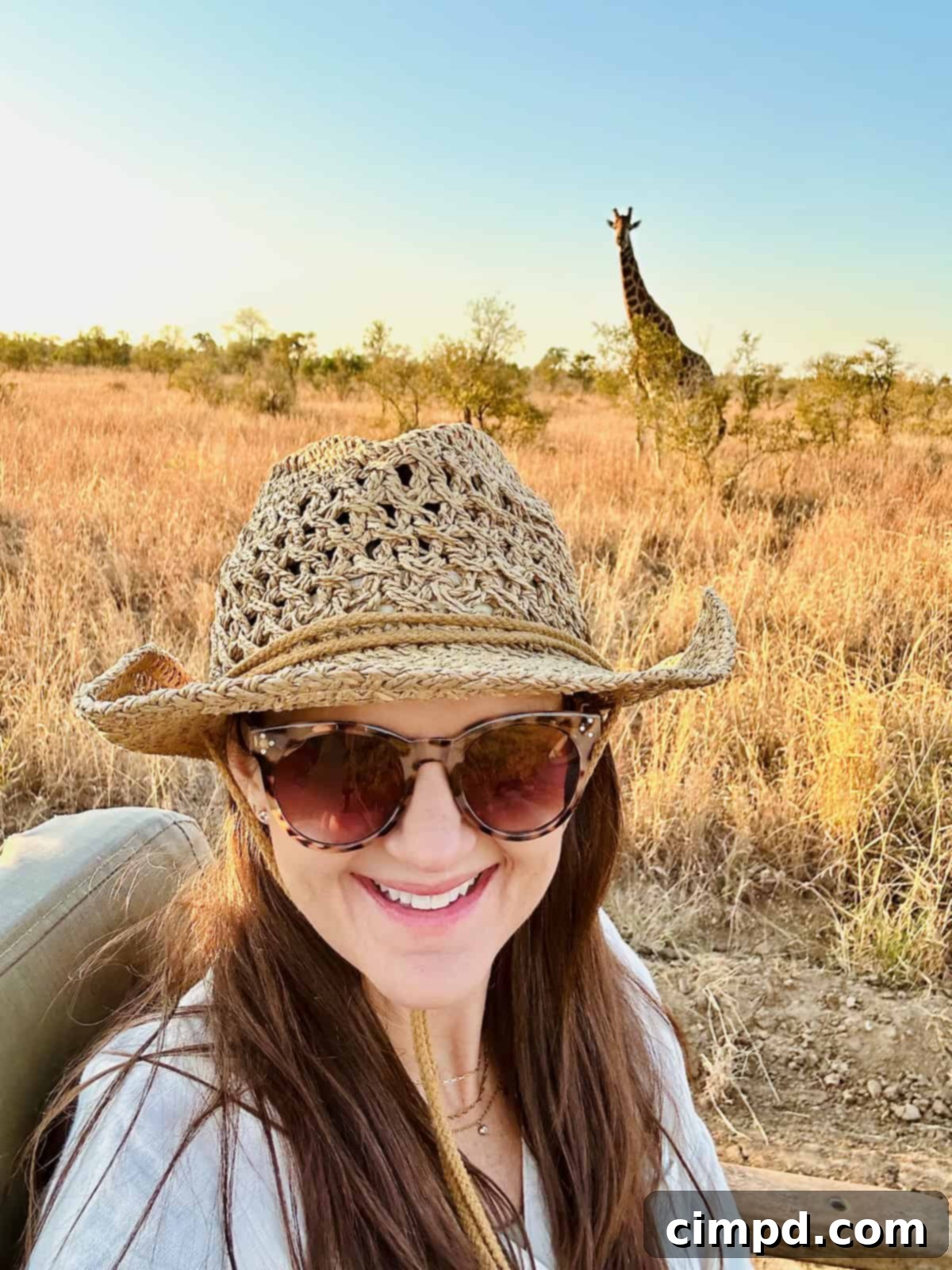 Exploring the Wonders of South Africa and Zambia 3 Maegan wearing a straw hat with a giraffe in the background during a safari.