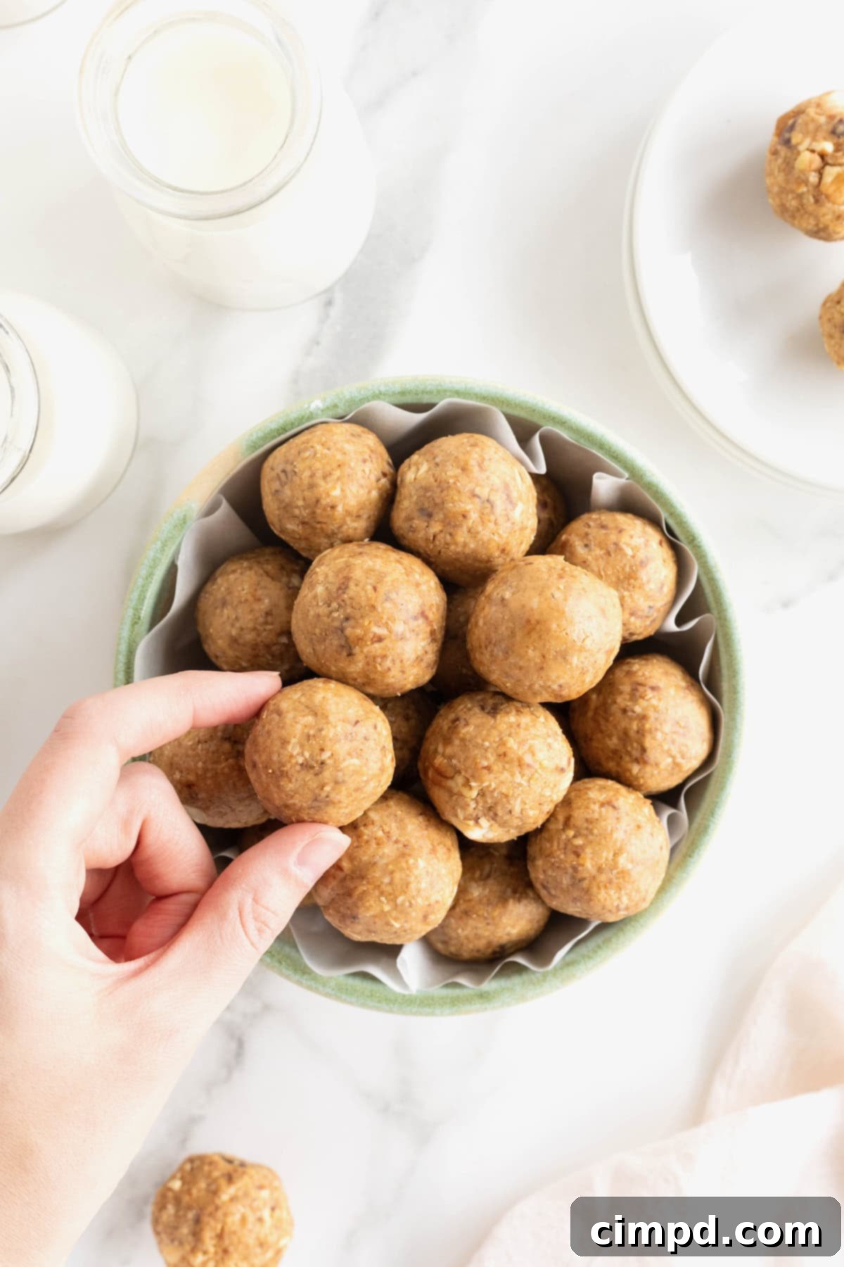 Wholesome Energy Bites 3 A hand removing a snack bite from a pale green earthenware serving bowl on a white marble counter.