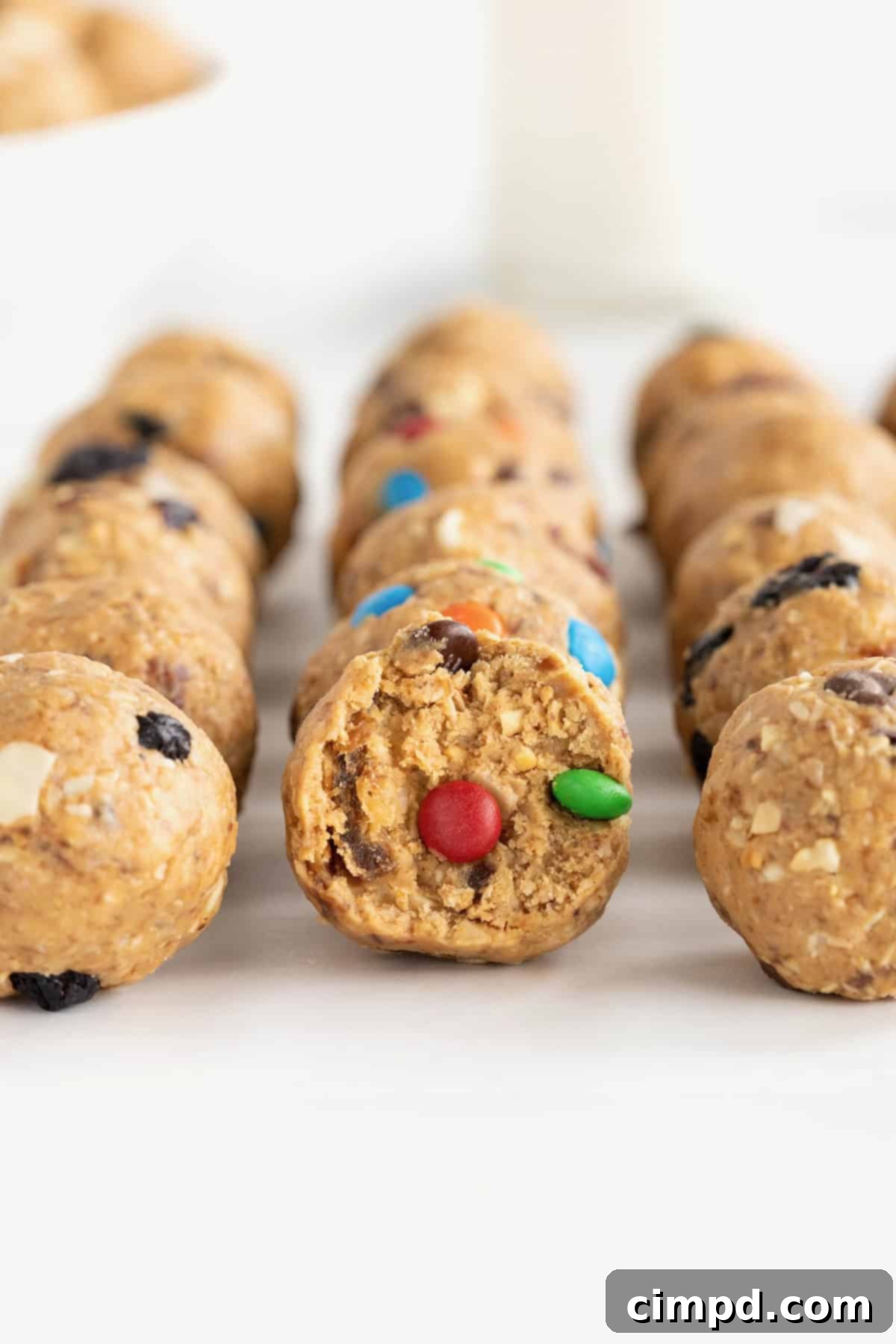 Wholesome Energy Bites 4 Energy bites with dried cranberries and white chocolate chips, mini M&Ms and dried blueberries on a white surface.