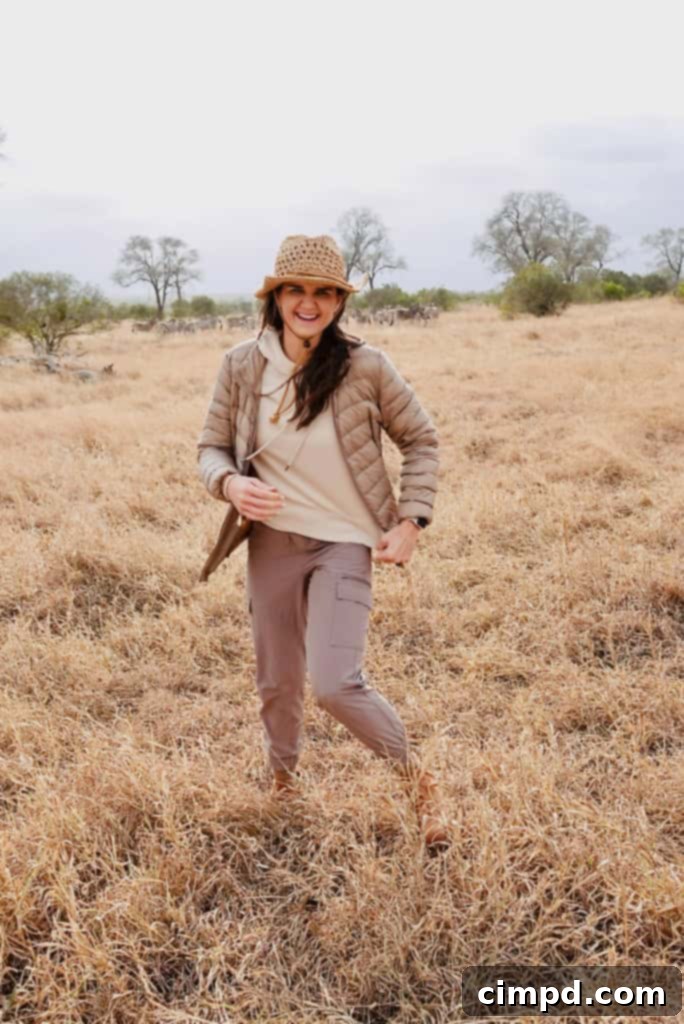 A woman wearing muted colors and a wide-brimmed hat, posing elegantly in the African bush.