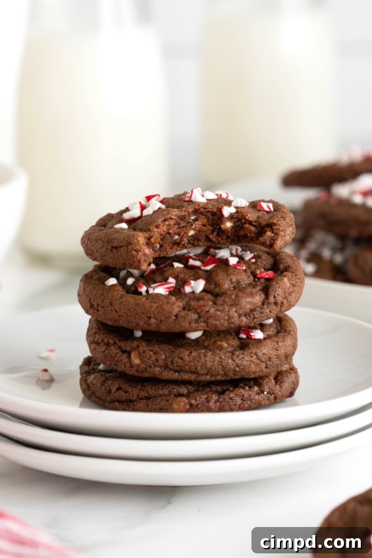 A perfectly arranged stack of four homemade chocolate peppermint cookies, adorned with festive crunch, resting on a clean white plate.