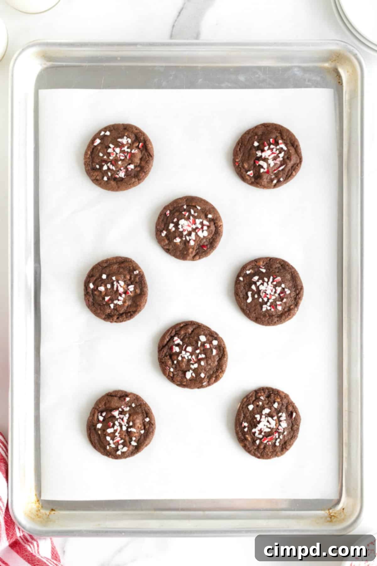 A pristine batch of eight freshly baked chocolate peppermint cookies, nestled on a parchment-lined aluminum baking sheet, ready for cooling.