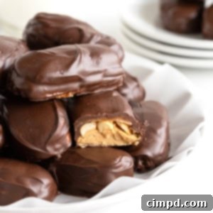 Chewy Homemade Snickers Treats 13 A pile of homemade Snickers bites on a parchment lined white plate. One of the candies has a bite out of it.