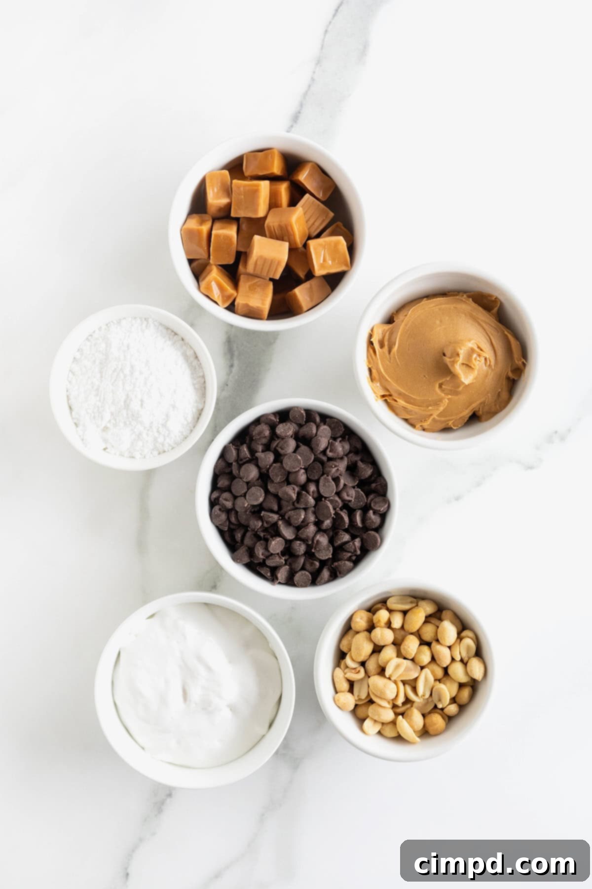 Chewy Homemade Snickers Treats 5 A vibrant display of fresh ingredients for homemade Snickers bites, meticulously arranged in small white dishes on a elegant white marble counter, ready for preparation.