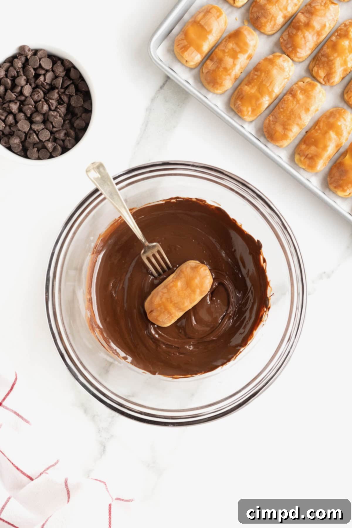 Chewy Homemade Snickers Treats 8 A homemade Snickers bite perfectly impaled on a metal fork, being carefully dipped into a rich pool of melted chocolate, illustrating the coating process.