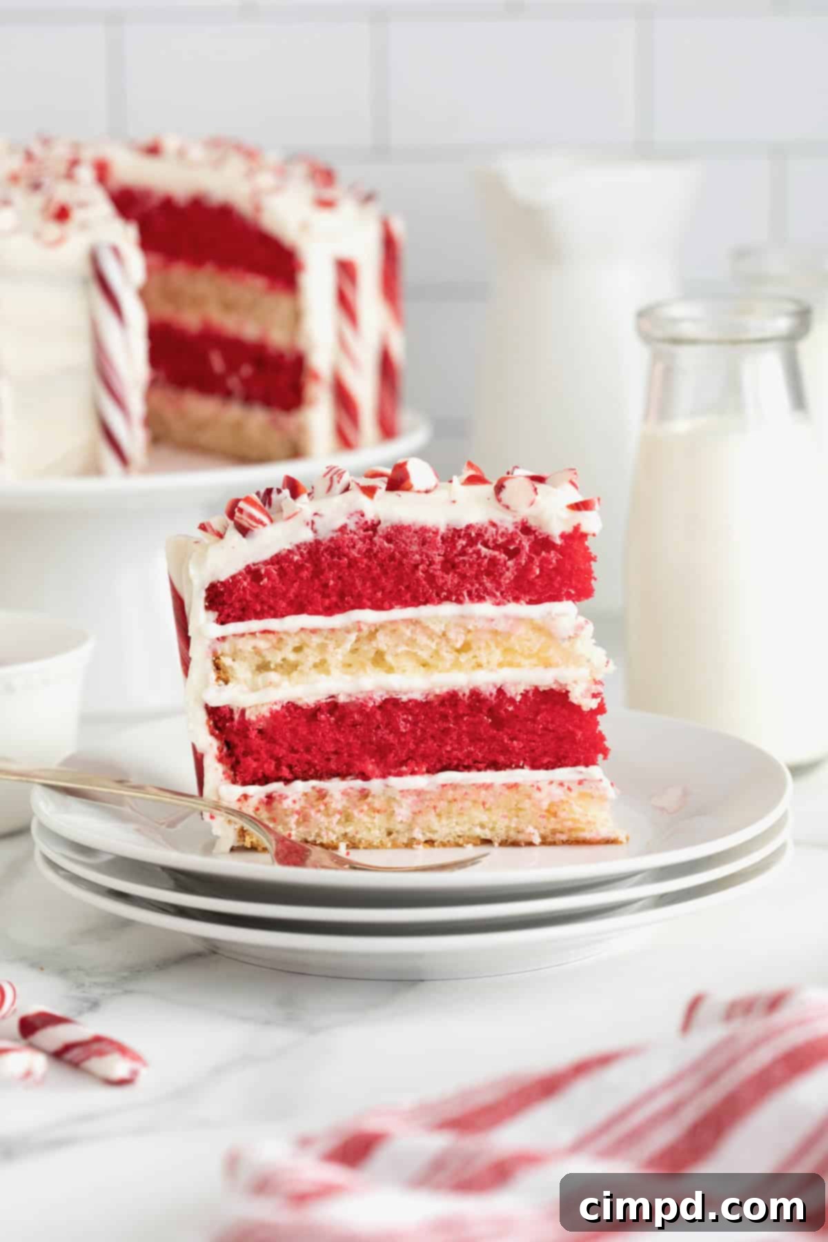 Peppermint Swirl Cake 2 A beautifully sliced red and white layered candy cane cake on a small white dessert plate, with a fork resting beside it, ready to be enjoyed.