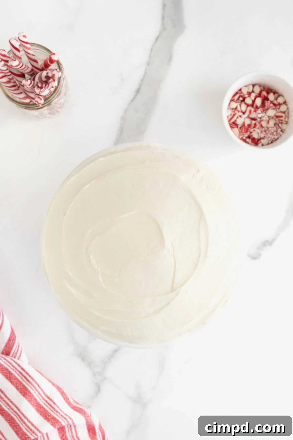 Peppermint Swirl Cake 11 A perfectly frosted round cake, glistening with white buttercream, resting elegantly on a pristine white marble counter, awaiting its final festive touches.