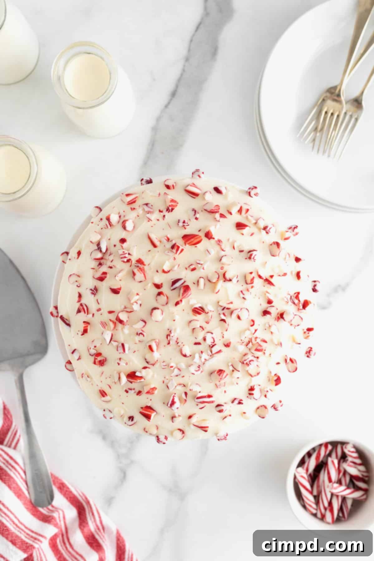 Peppermint Swirl Cake 12 A pristine white-frosted round cake, artfully adorned with shimmering peppermint pieces, creating a delightful and festive visual texture.