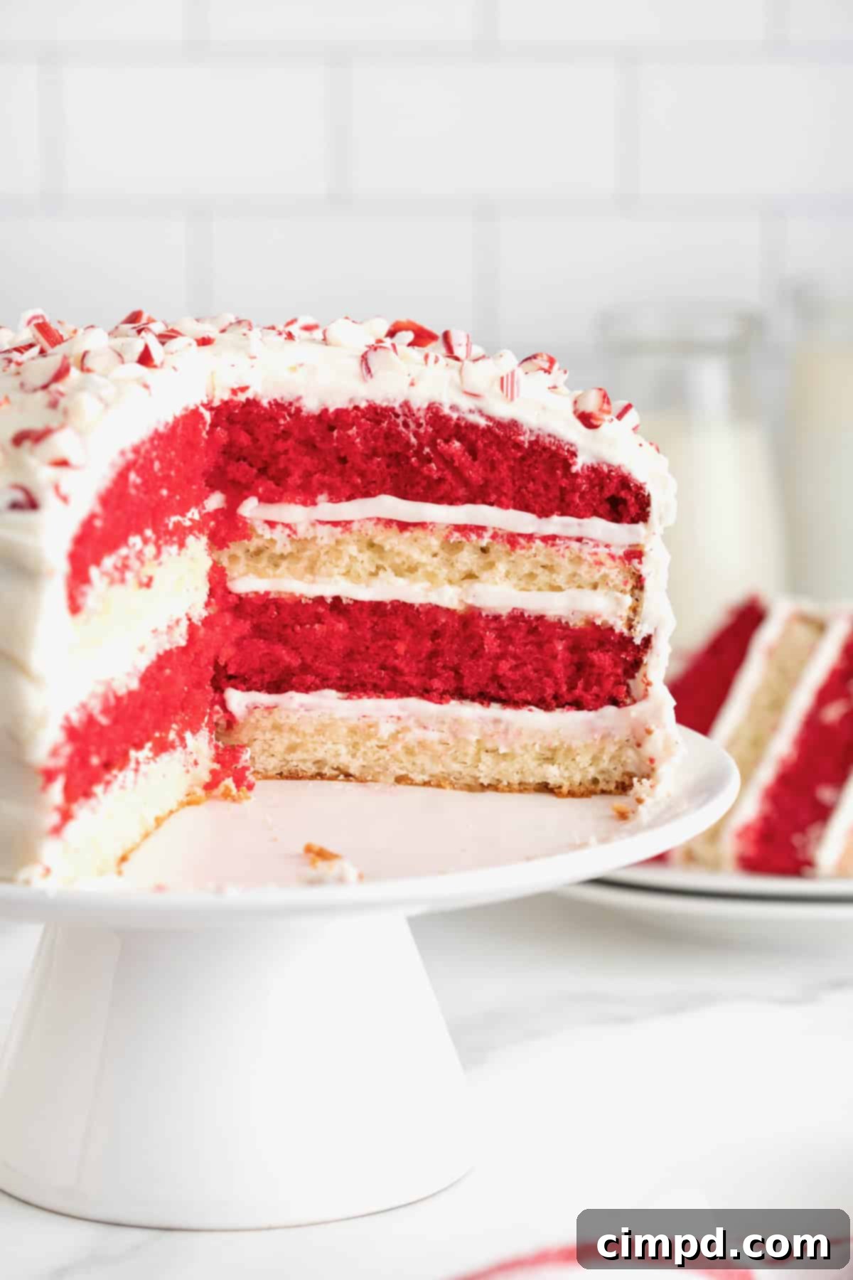 Peppermint Swirl Cake 14 A stunning round cake featuring alternating layers of festive red and pristine white, beautifully frosted in white and adorned with delicate peppermint bits scattered on top.