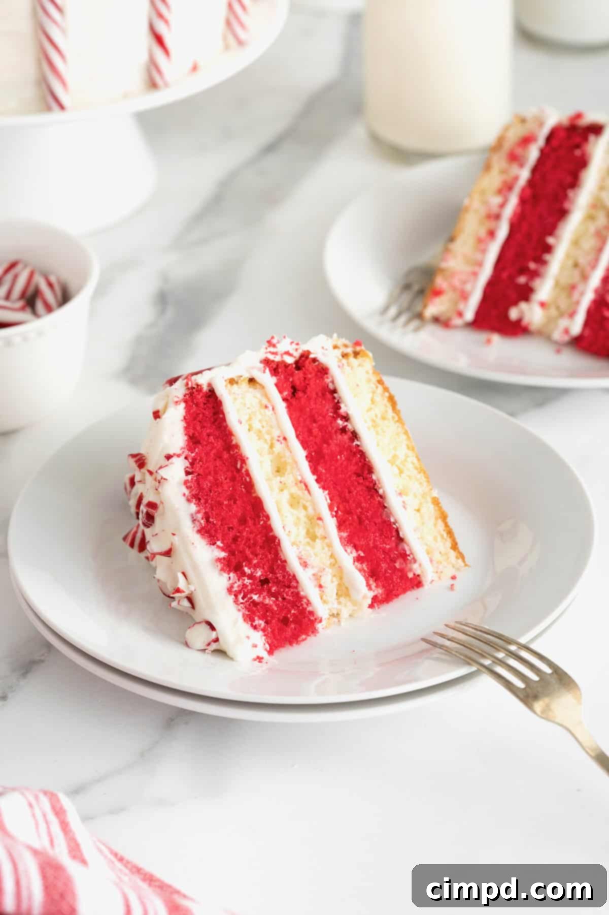 Peppermint Swirl Cake 5 Two exquisite slices of candy cane cake, elegantly presented on small white dessert plates atop a luxurious white marble counter. Forks are perfectly poised on the plates, ready for indulgence.