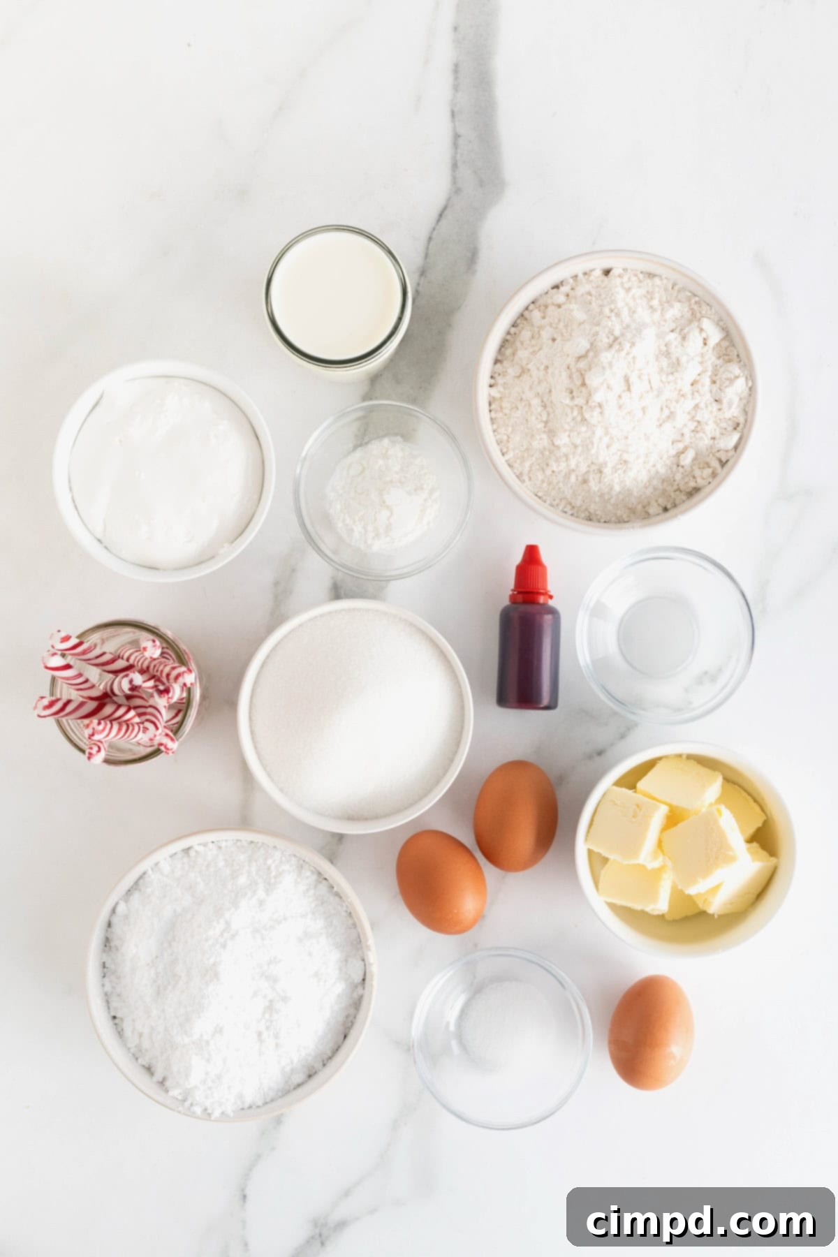 Peppermint Swirl Cake 6 A collection of precisely measured ingredients, arranged in small white glass dishes on a pristine white marble counter, ready for the creation of a delicious candy cane cake.