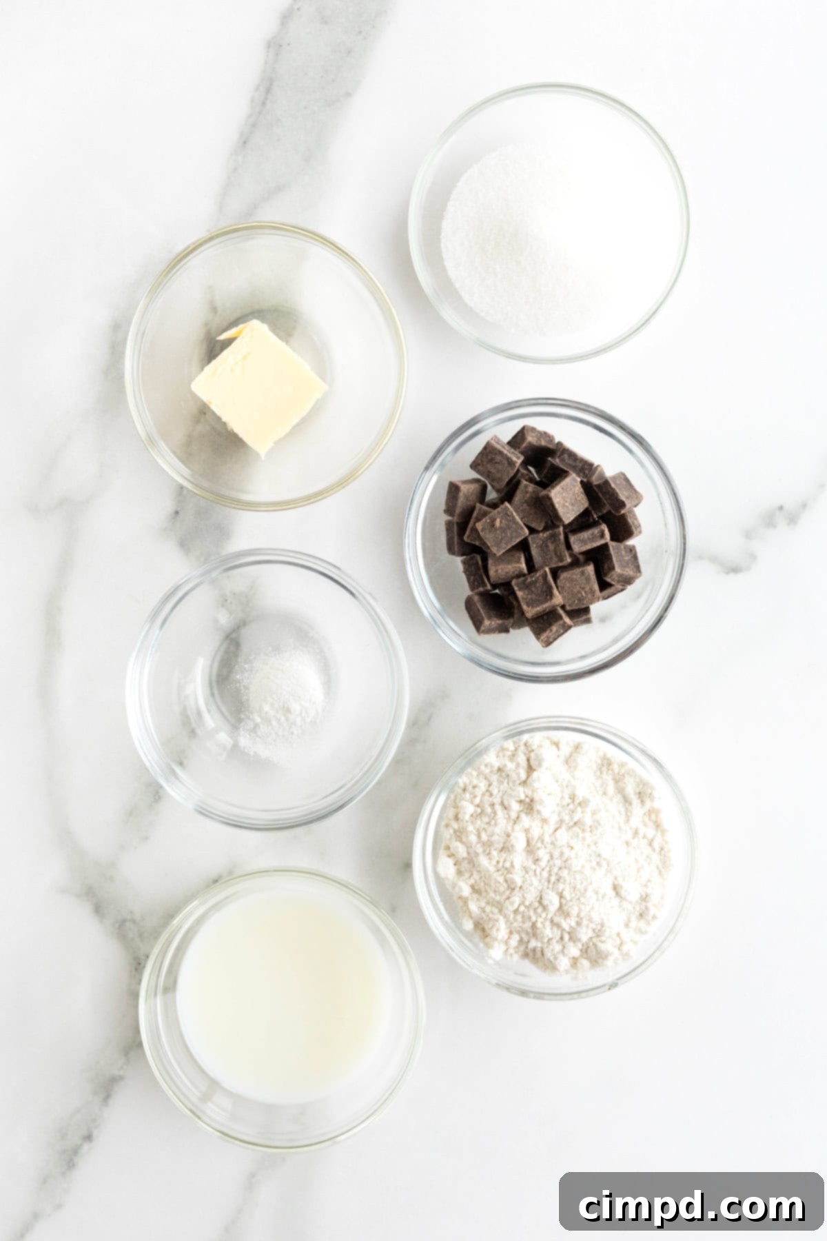 Speedy Chocolate Mug Brownie 5 Individual ingredients for a microwave brownie in a mug, neatly arranged in small glass containers on a clean white marble counter, ready for assembly.