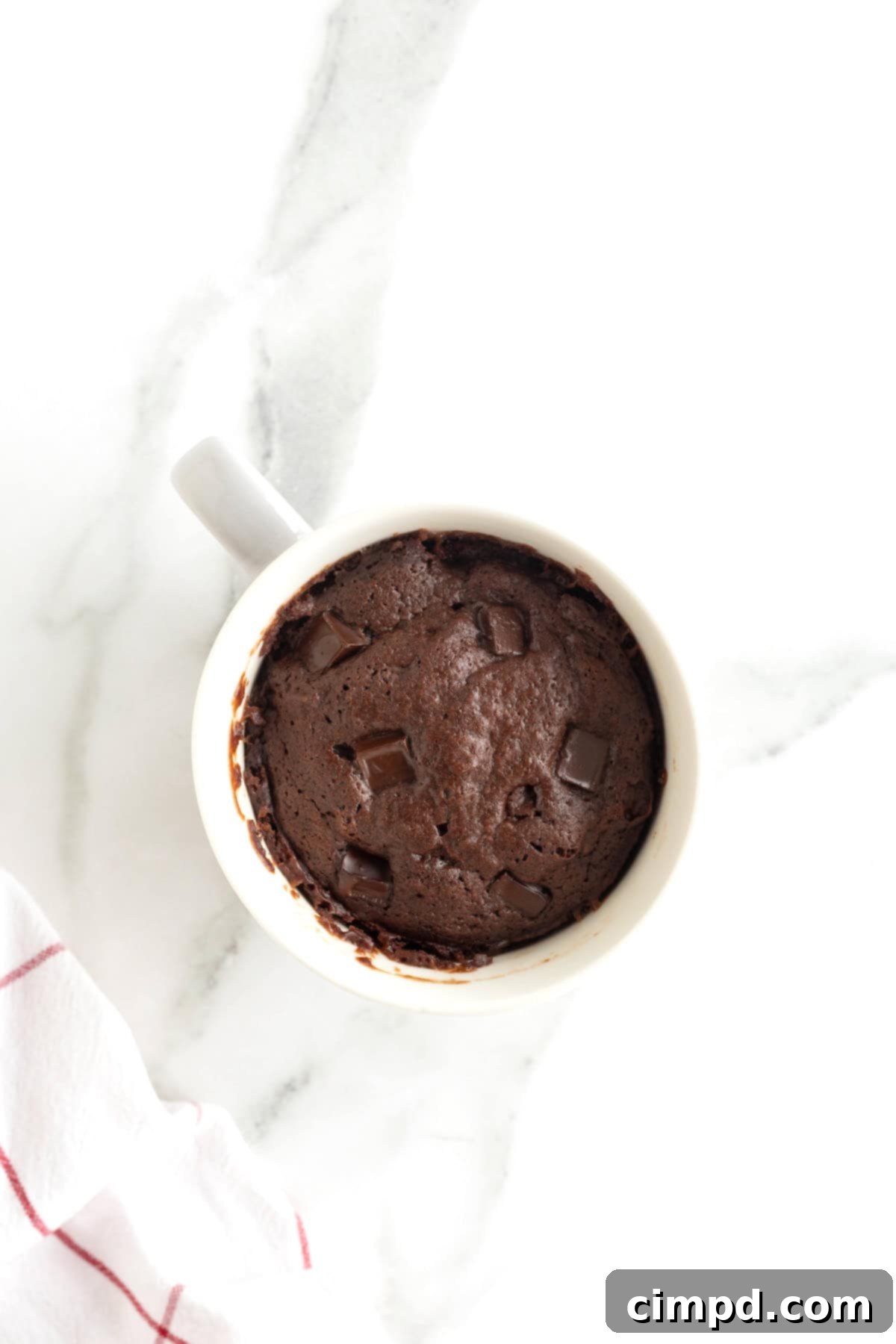 Speedy Chocolate Mug Brownie 7 A perfectly cooked, warm brownie nestled in a white mug, ready for toppings, sitting on a cool white marble counter.