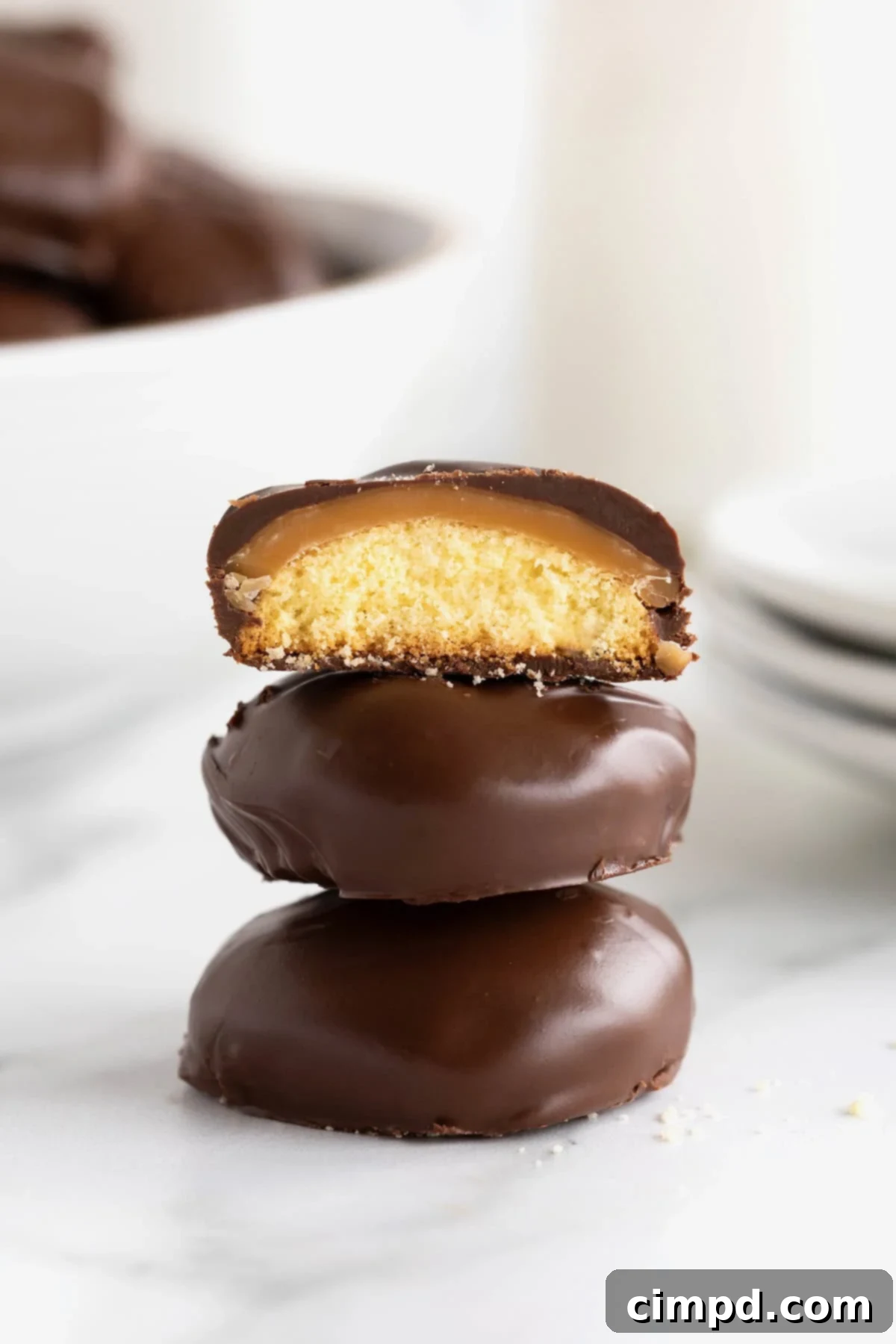 Three Twix Bites in a stack on a white marble counter. The top bite is cut in half to reveal the cookie, caramel and chocolate layers.