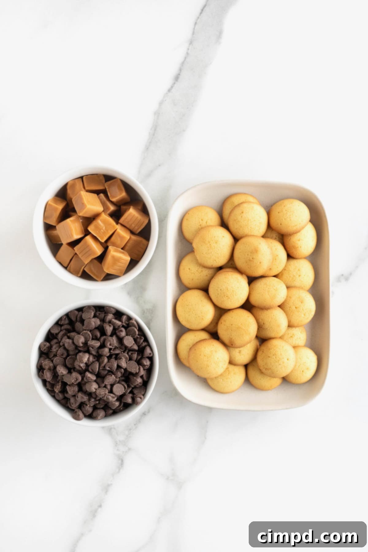 Ingredients to make Twix Bites in white dishes on a white marble counter.