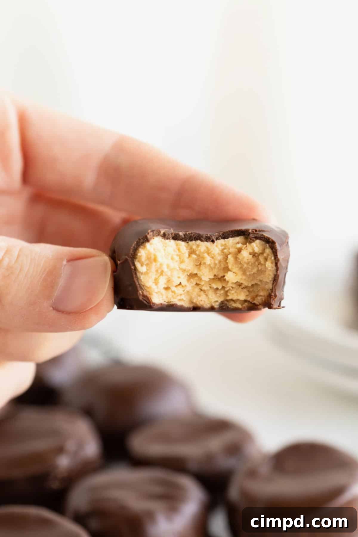Three Ingredient Peanut Butter Cups 3 A hand delicately holding a single, perfectly formed homemade peanut butter cup between the thumb and forefinger, showcasing its smooth chocolate coating.
