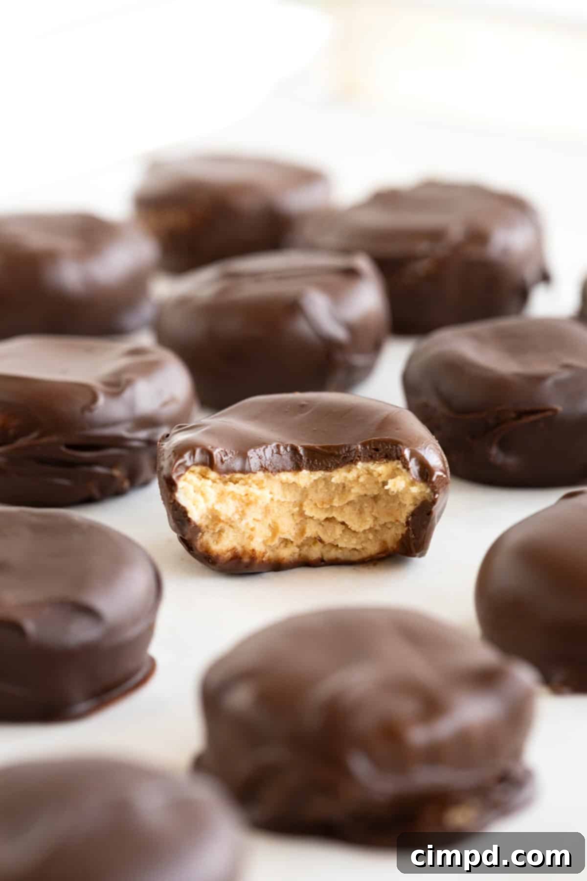 Three Ingredient Peanut Butter Cups 5 A plentiful serving of homemade peanut butter cups arranged on a parchment-lined metal cooling rack, capturing their golden-brown peanut butter centers peaking through the chocolate.
