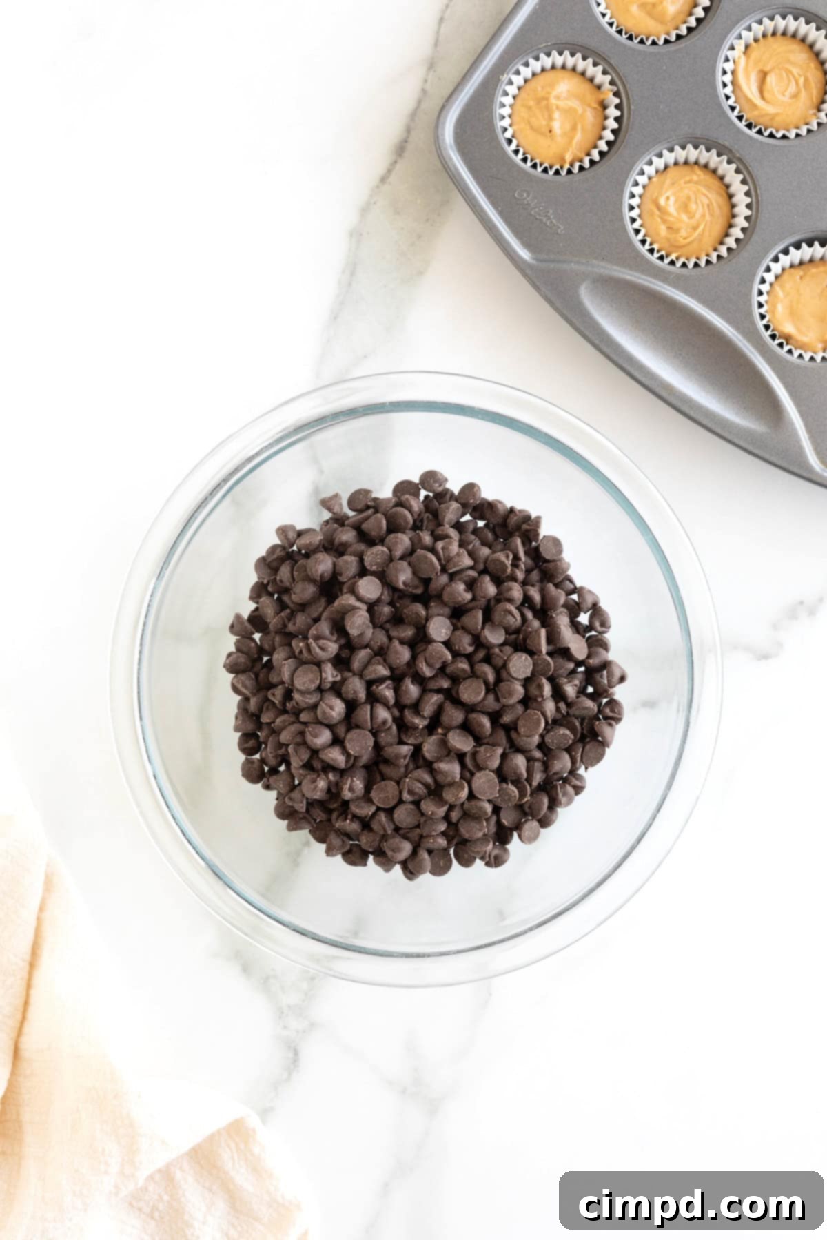 Three Ingredient Peanut Butter Cups 8 A generous quantity of semi-sweet chocolate chips resting in a medium-sized glass mixing bowl on a pristine white marble countertop, ready for melting.