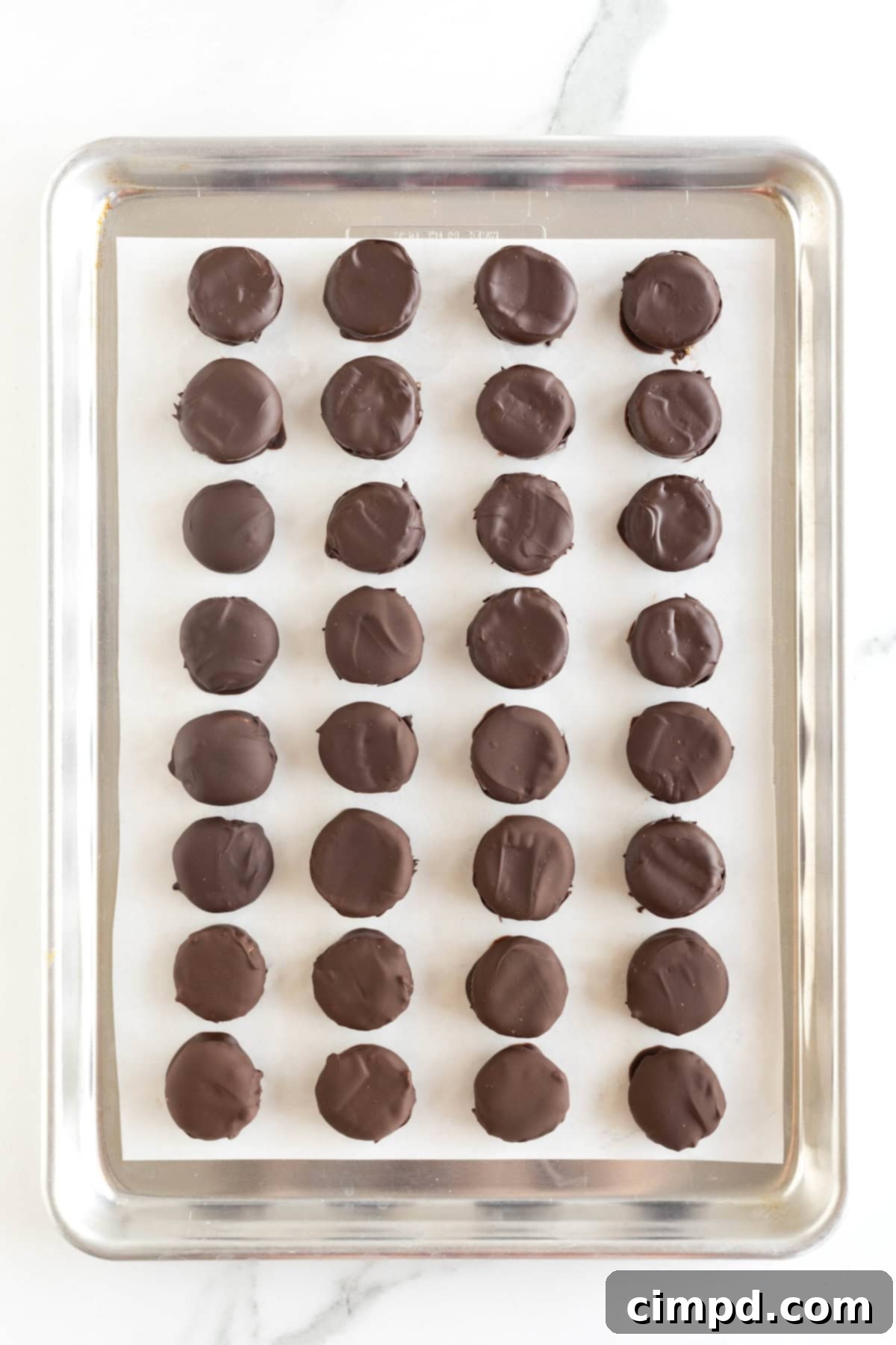 Three Ingredient Peanut Butter Cups 10 A beautiful display of 32 homemade peanut butter cups perfectly arranged on a parchment-lined baking sheet, resting on a white marble countertop.