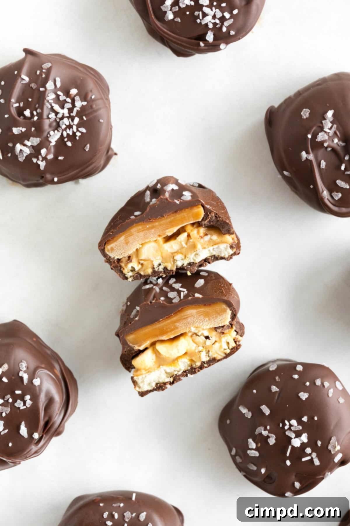 A Take 5 Candy Bar Bite cut in half on a parchment lined baking tray. Visible are a pretzel topped with peanuts and peanut butter, caramel and chocolate.