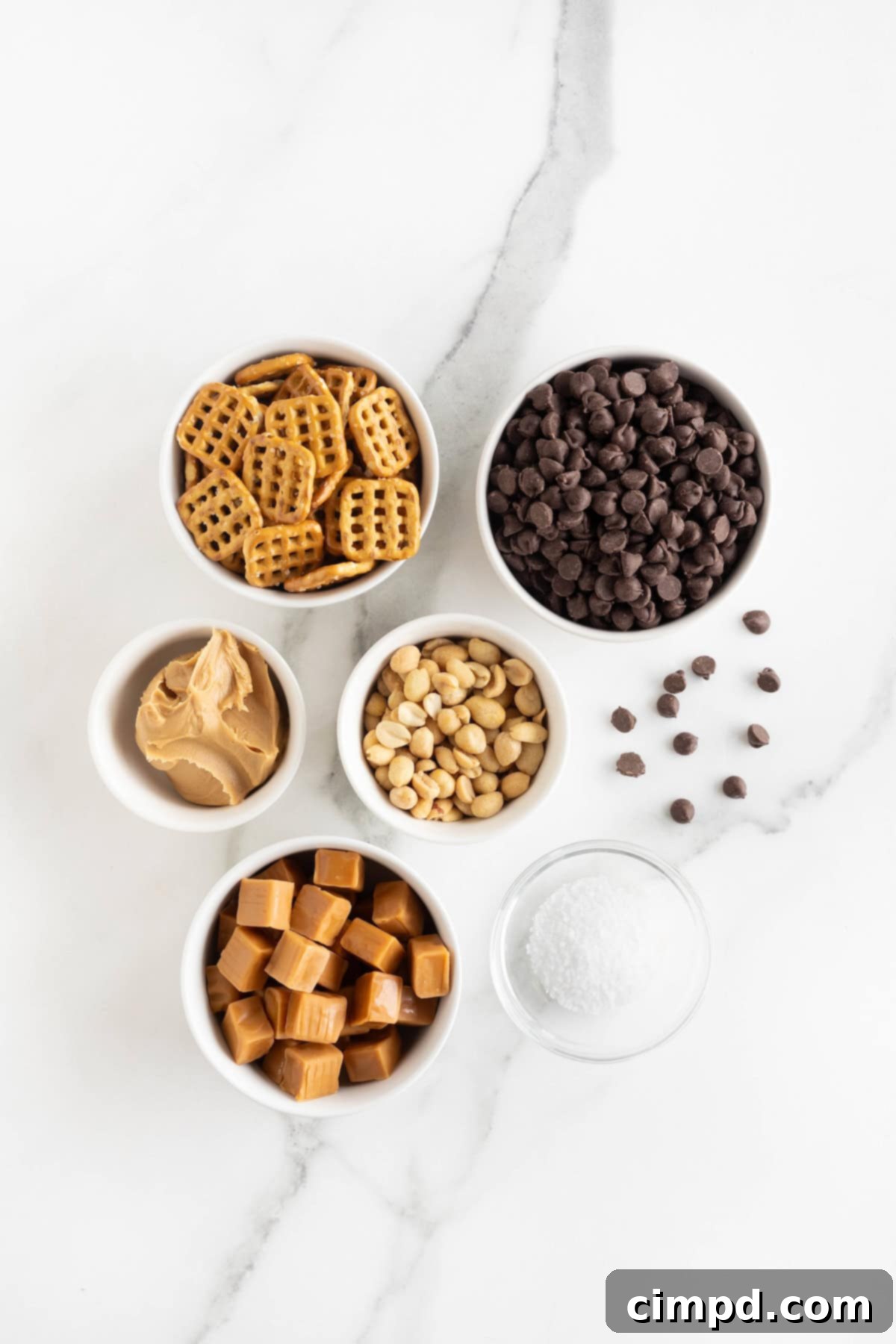 Ingredients to make Take 5 Candy Bar Bites in small white glass dishes on a white marble counter.