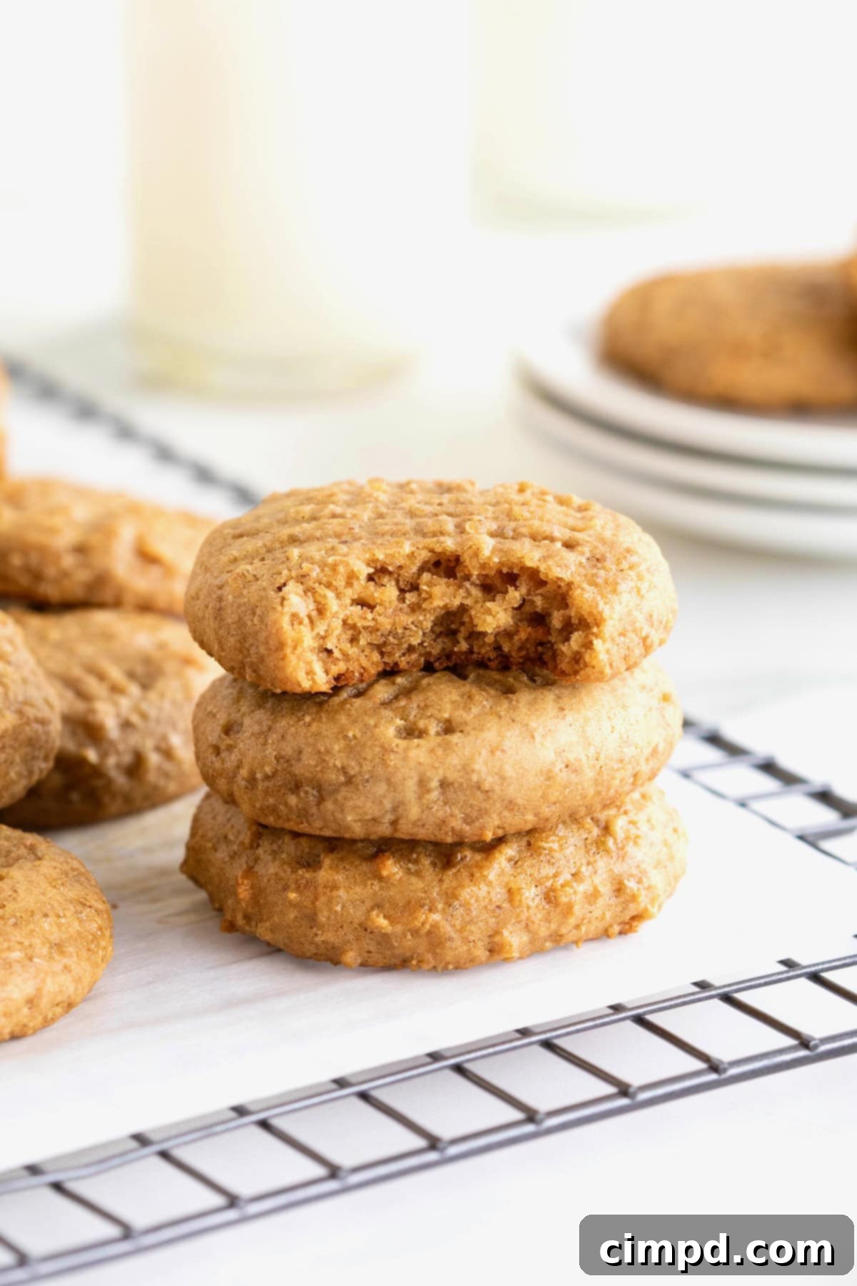 Wholesome Peanut Butter Quinoa Cookies 3 Three perfectly baked peanut butter quinoa cookies stacked on a parchment-lined cooling rack. The top cookie has a tempting bite taken out, revealing its soft interior and quinoa bits.